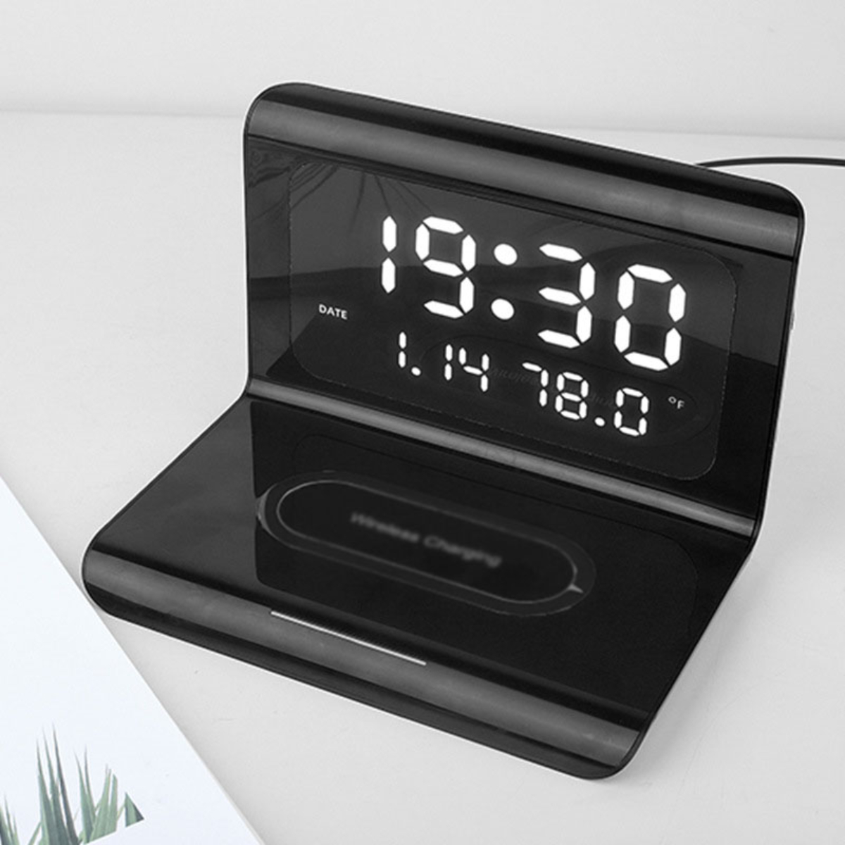 Schwarze Digitaluhr, die Zeit und Datum anzeigt. Sie hat eine kabellose Ladestation.