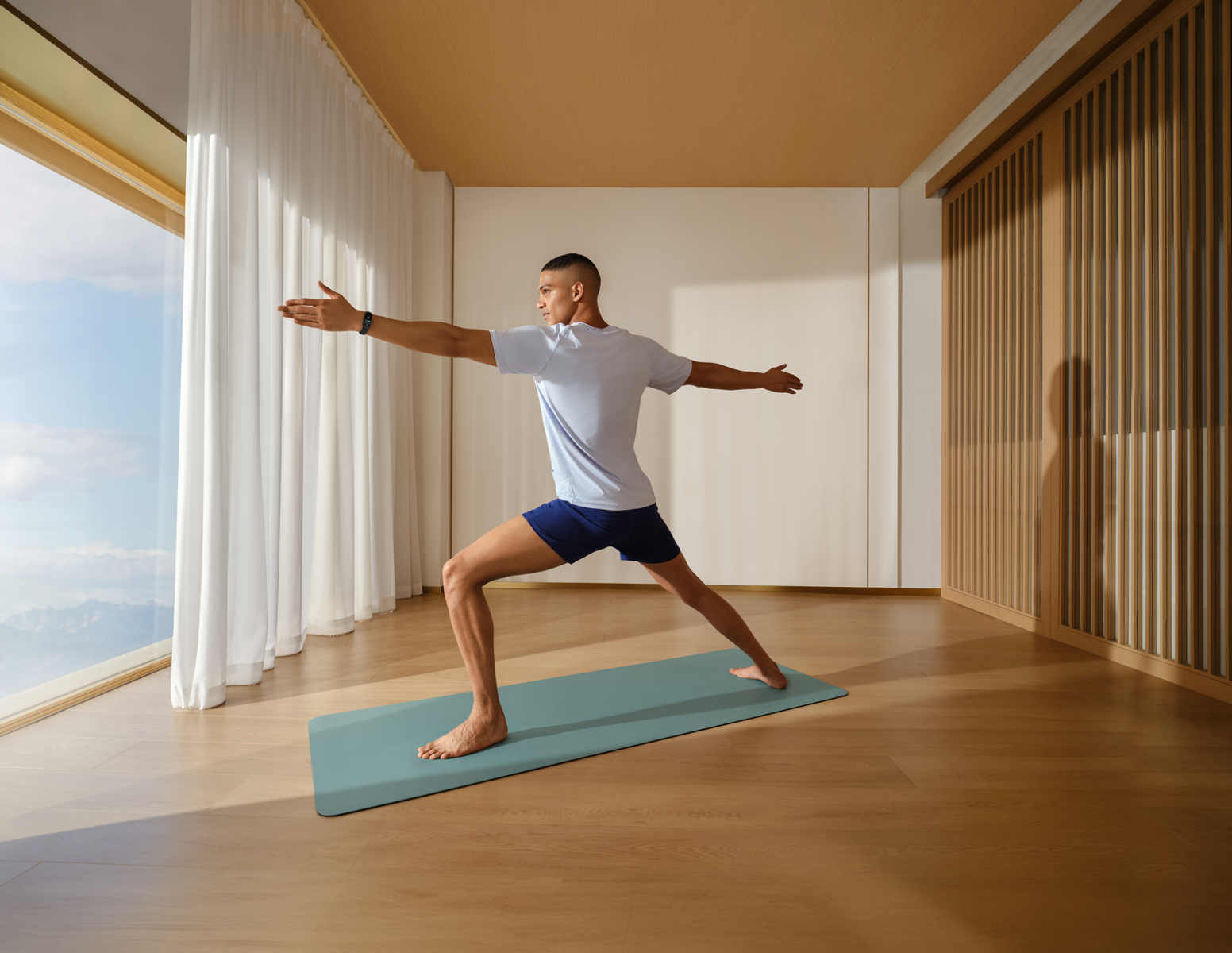 Mężczyzna w pozycji jogi na macie w jasnym pokoju. Ręce wyciągnięte, jedna noga do przodu.