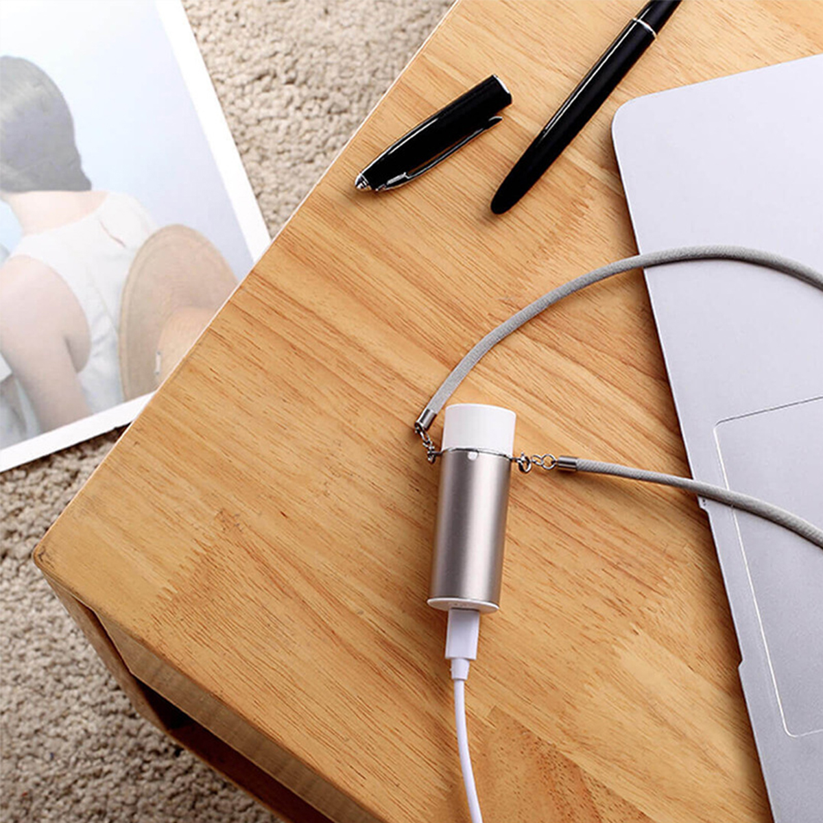 Schreibtisch mit Laptop, Stift und Ladegerät, das mit einem Kabel verbunden ist. Holzoberfläche.
