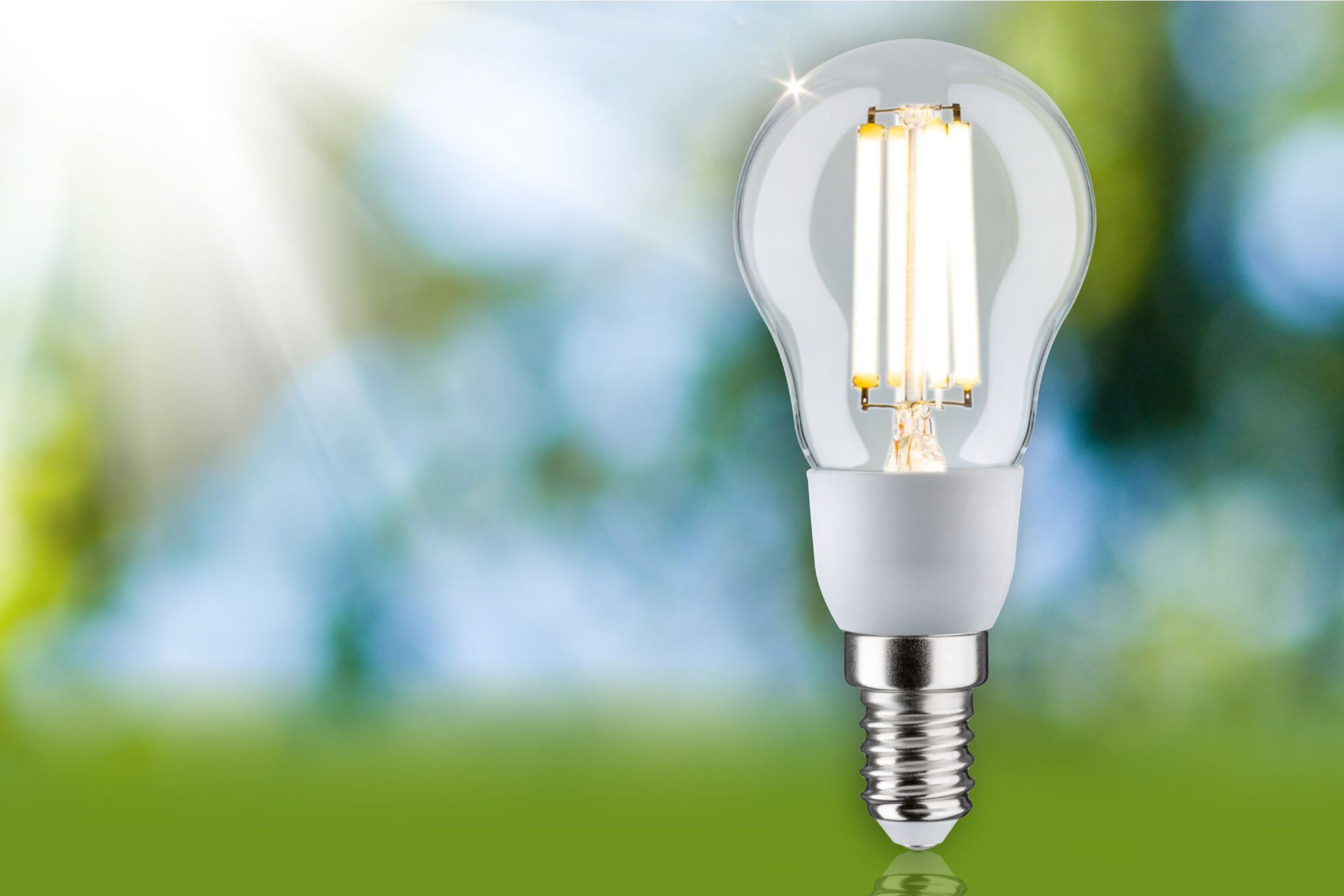 LED-Glühbirne mit klarem Glas. Sie ist beleuchtet, mit einem verschwommenen grünen und blauen Hintergrund.