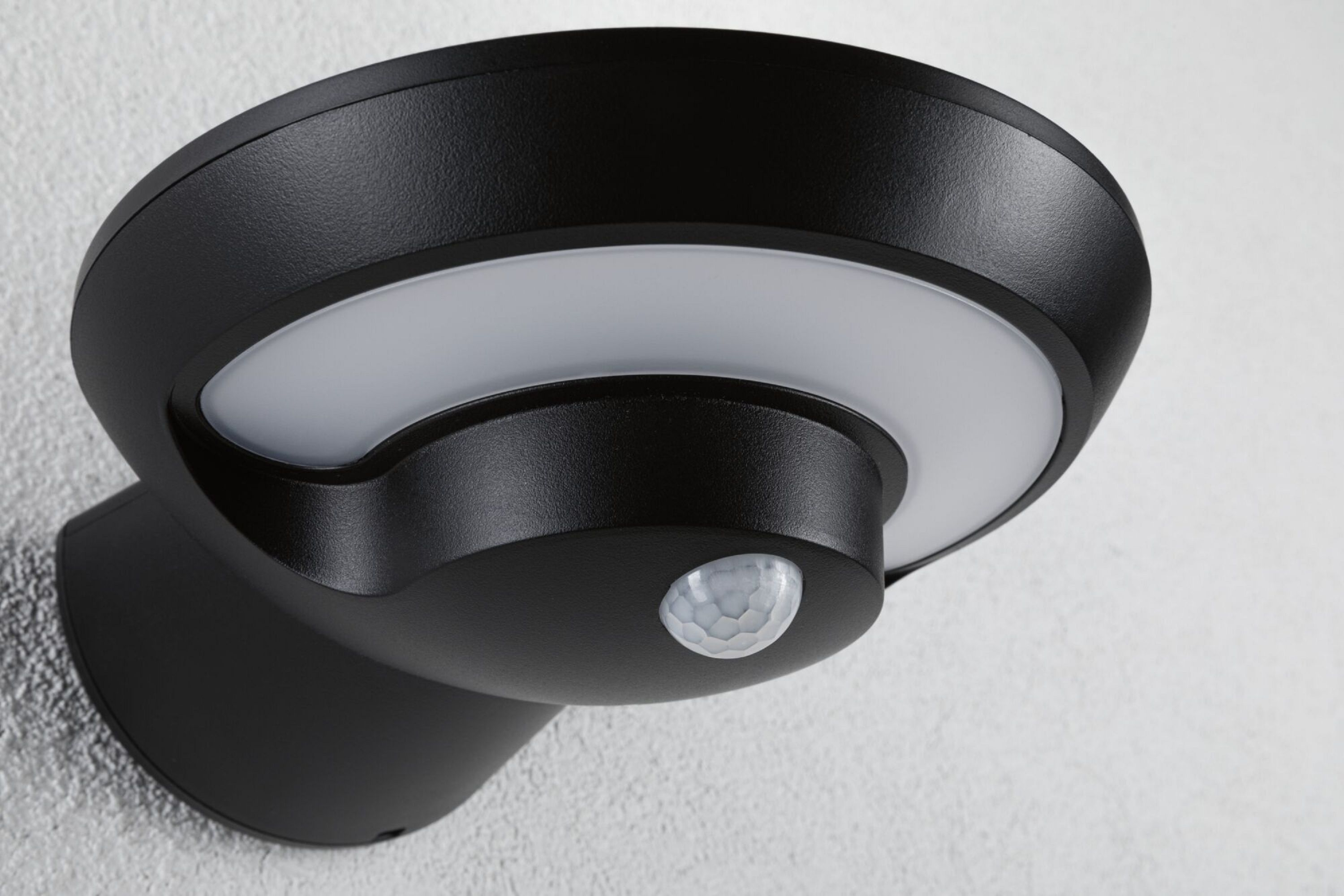 Czarna zewnętrzna lampa ścienna z białym pierścieniem świetlnym i czujnikiem ruchu.