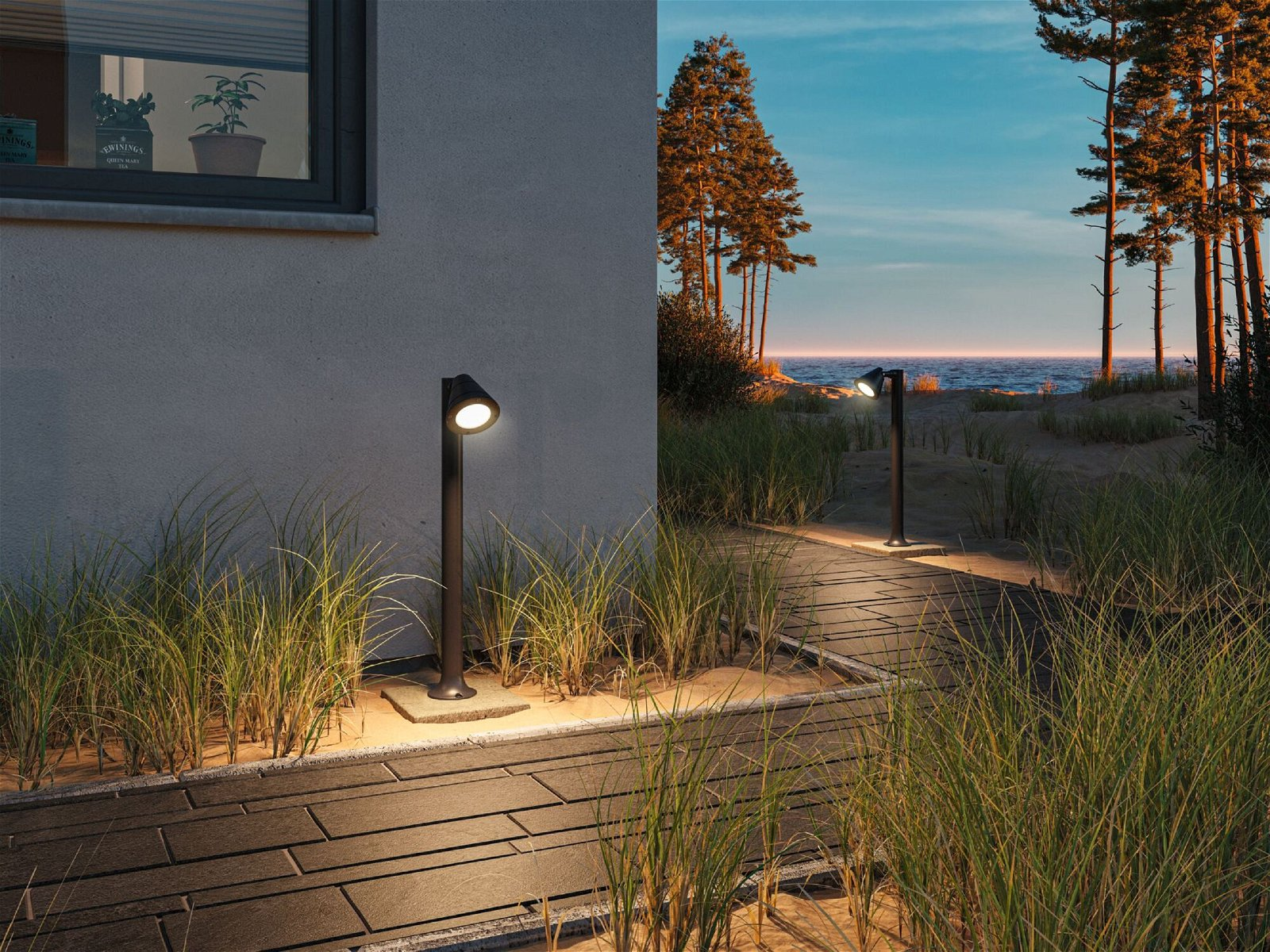 Scena na zewnątrz o zmierzchu z dwoma czarnymi lampami na słupach oświetlających ścieżkę i plażę.
