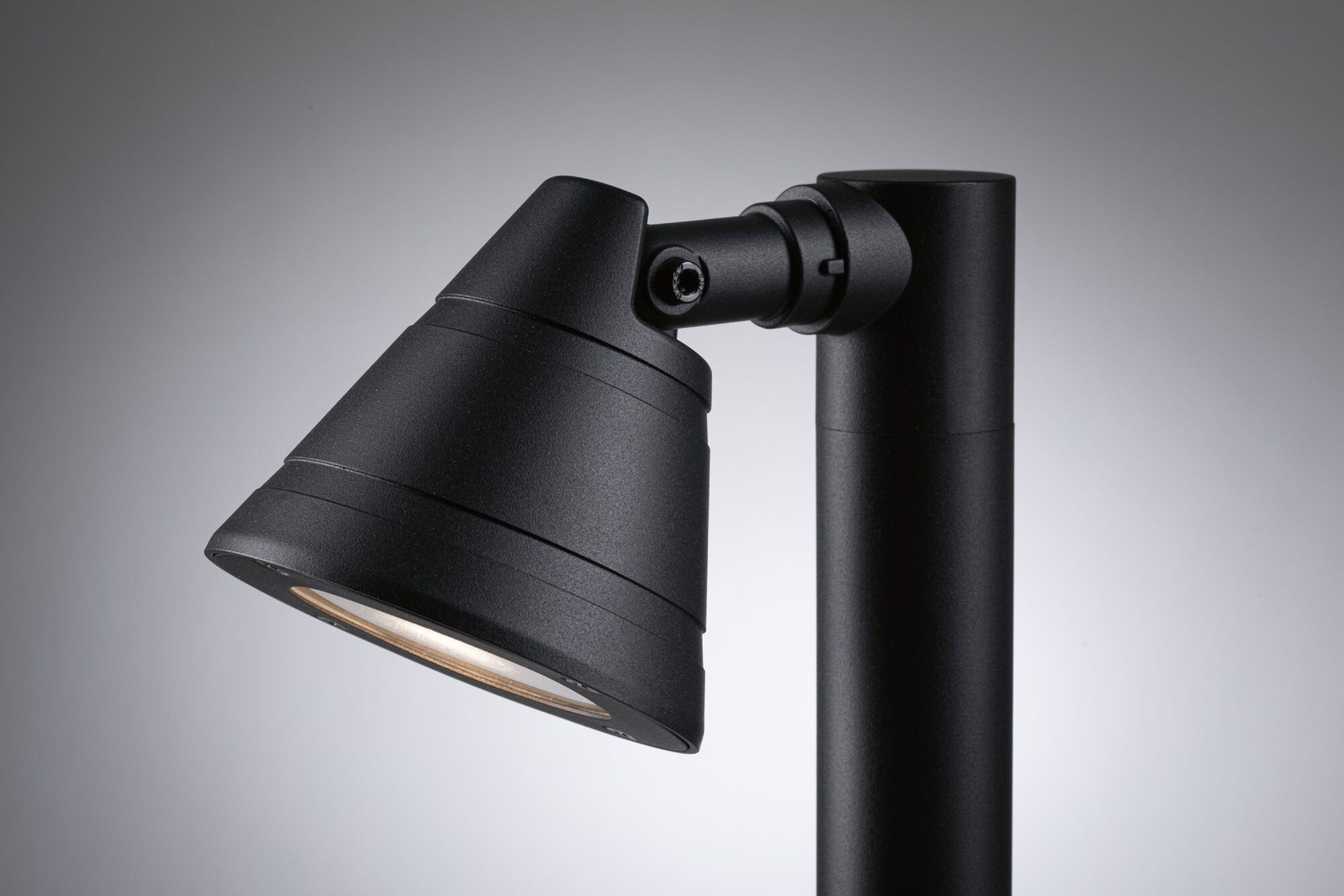 Czarny reflektor zewnętrzny zamontowany na słupie, skierowany w stronę światła.
