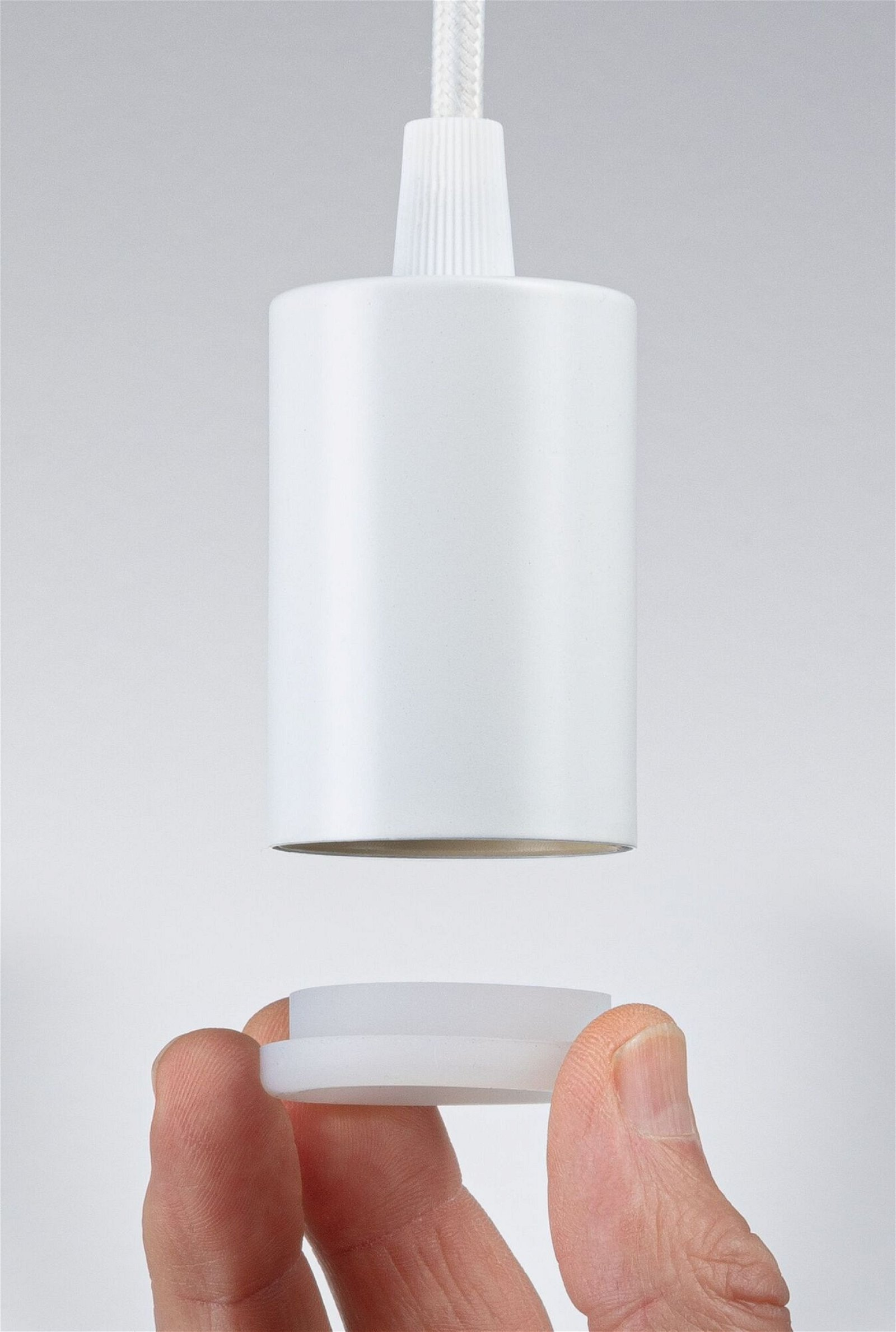 Biała oprawa oświetleniowa. Ręka trzyma jej część, gotową do połączenia. Tło jest jasnoszare.