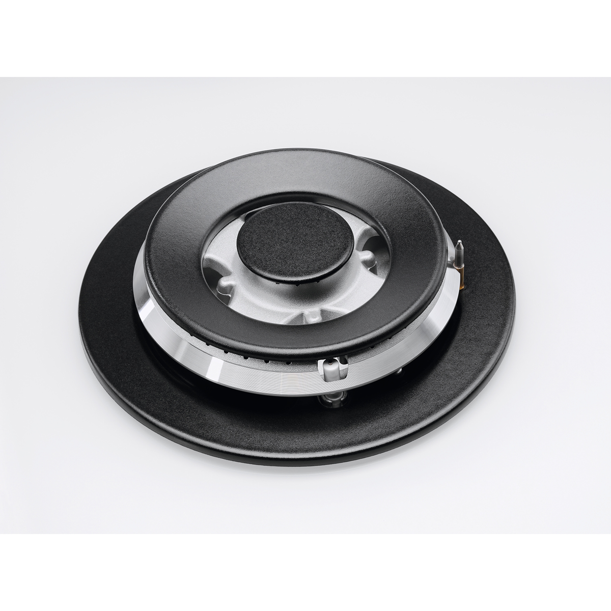 Zbliżenie czarnego palnika kuchenki gazowej ze srebrnym metalowym środkiem. Tło jest białe.