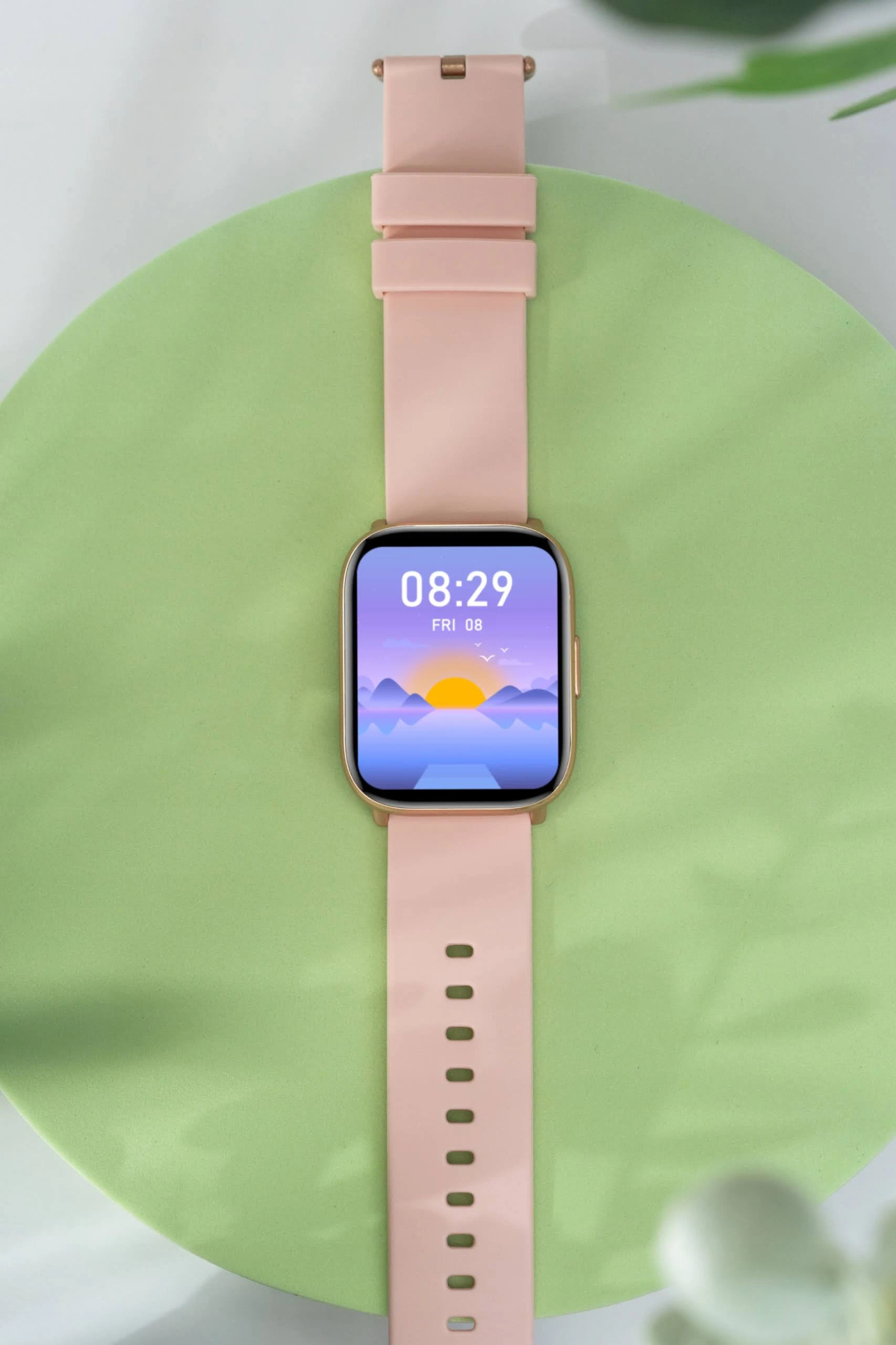 Złoty smartwatch z różowym paskiem. Ekran wyświetla godzinę i scenę wschodu słońca.