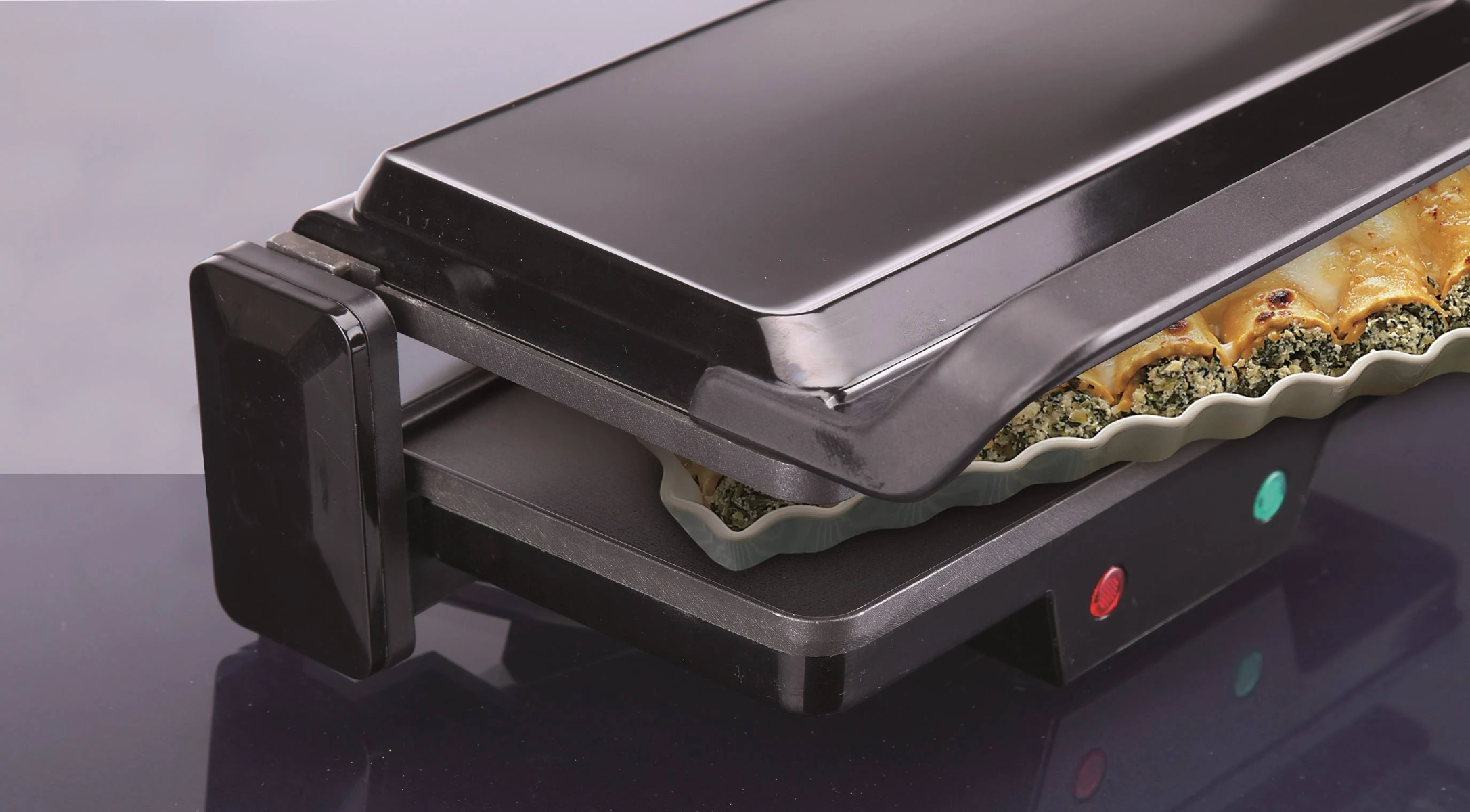 Czarny grill elektryczny z białym naczyniem w środku, z jedzeniem. Pokrywa jest zamknięta.