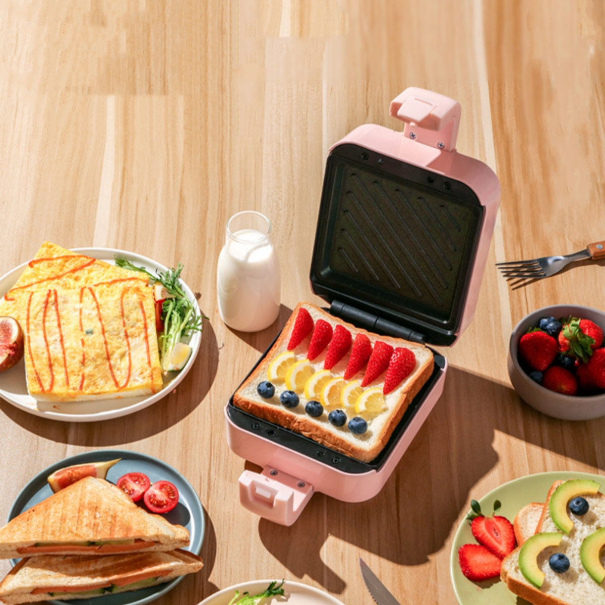 Rosa Sandwichmaker mit Sandwich, Erdbeeren, Blaubeeren und Milch auf einem Holztisch.