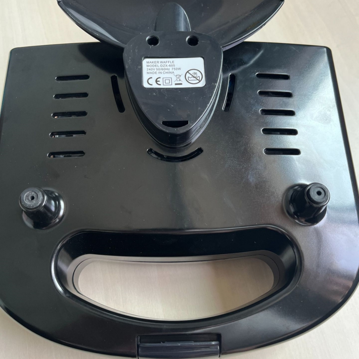 Unteransicht eines schwarzen Waffeleisens. Griff und Details sichtbar. Etikett in der Mitte.