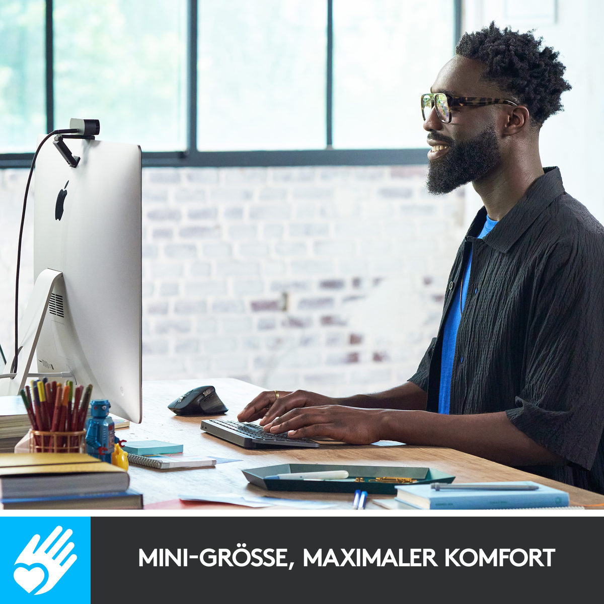 Mężczyzna piszący na klawiaturze, komputerze, monitorze, myszy i kamerze internetowej na drewnianym biurku. Mężczyzna w okularach.