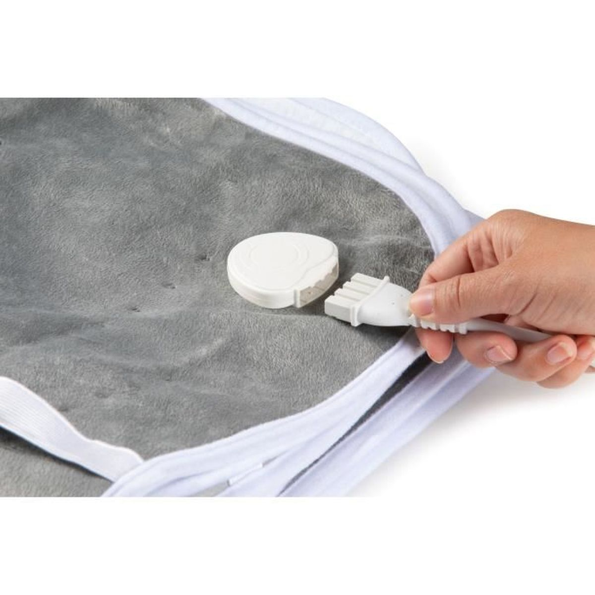 Una mano tiene una spina bianca collegata a una coperta grigia riscaldata. È visibile un quadrante di controllo bianco.