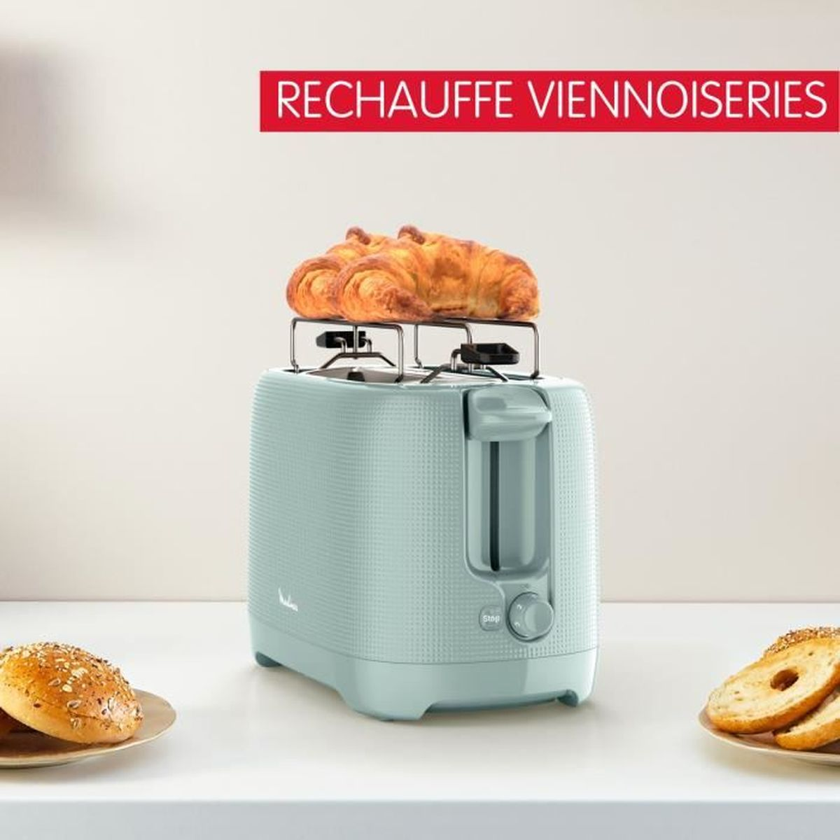 Ein türkisfarbener Toaster mit Croissants oben drauf und Brötchen an der Seite.