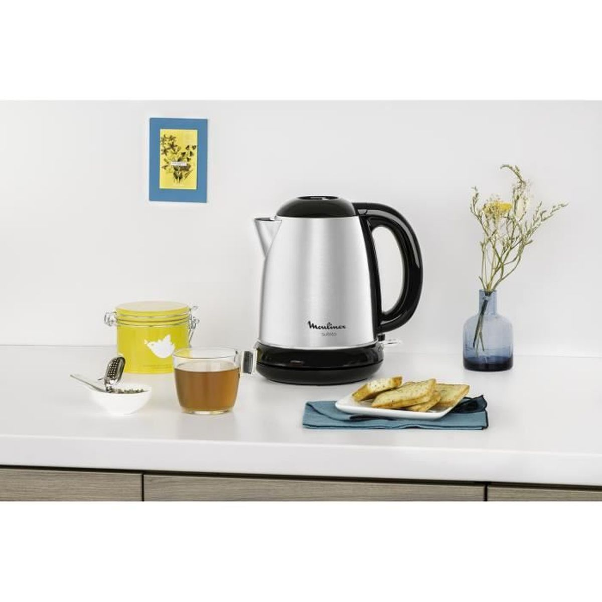 Czajnik, herbata, chleb i kwiaty ułożone na białym blacie.