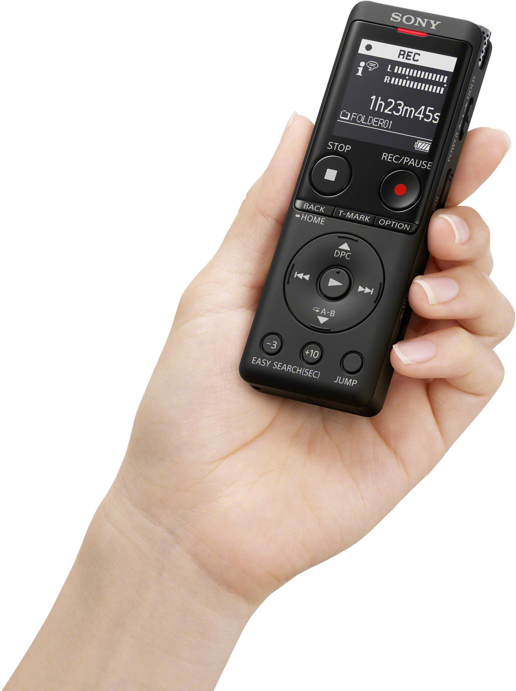 Dłoń trzymająca czarny rejestrator audio. Wyświetlacz pokazuje czas nagrywania i opcje. Białe tło.