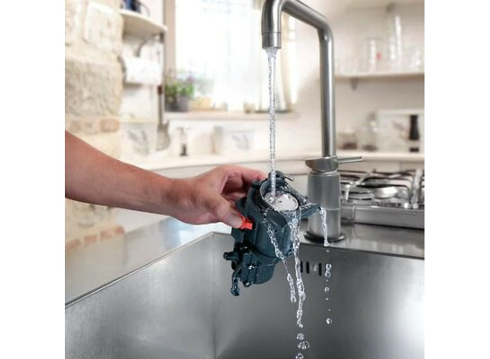 Hand hält ein Teil einer Kaffeemaschine unter einem Wasserhahn. Wasser fließt.