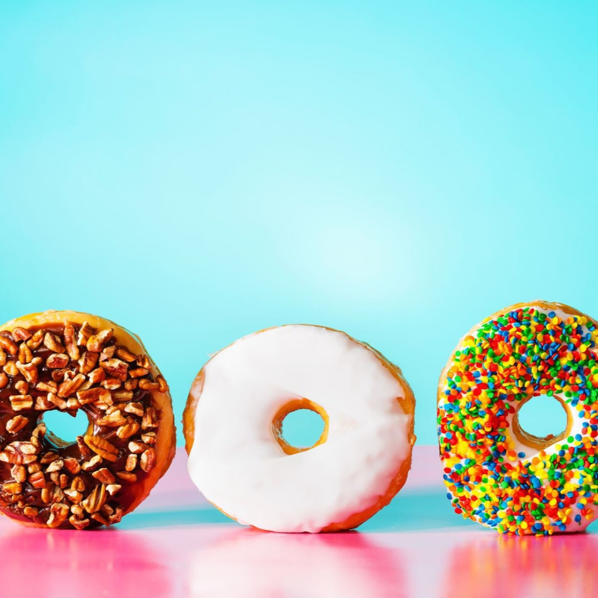 Drei Donuts: einer mit Pekannüssen, einer mit weißem Zuckerguss, einer mit Streuseln.