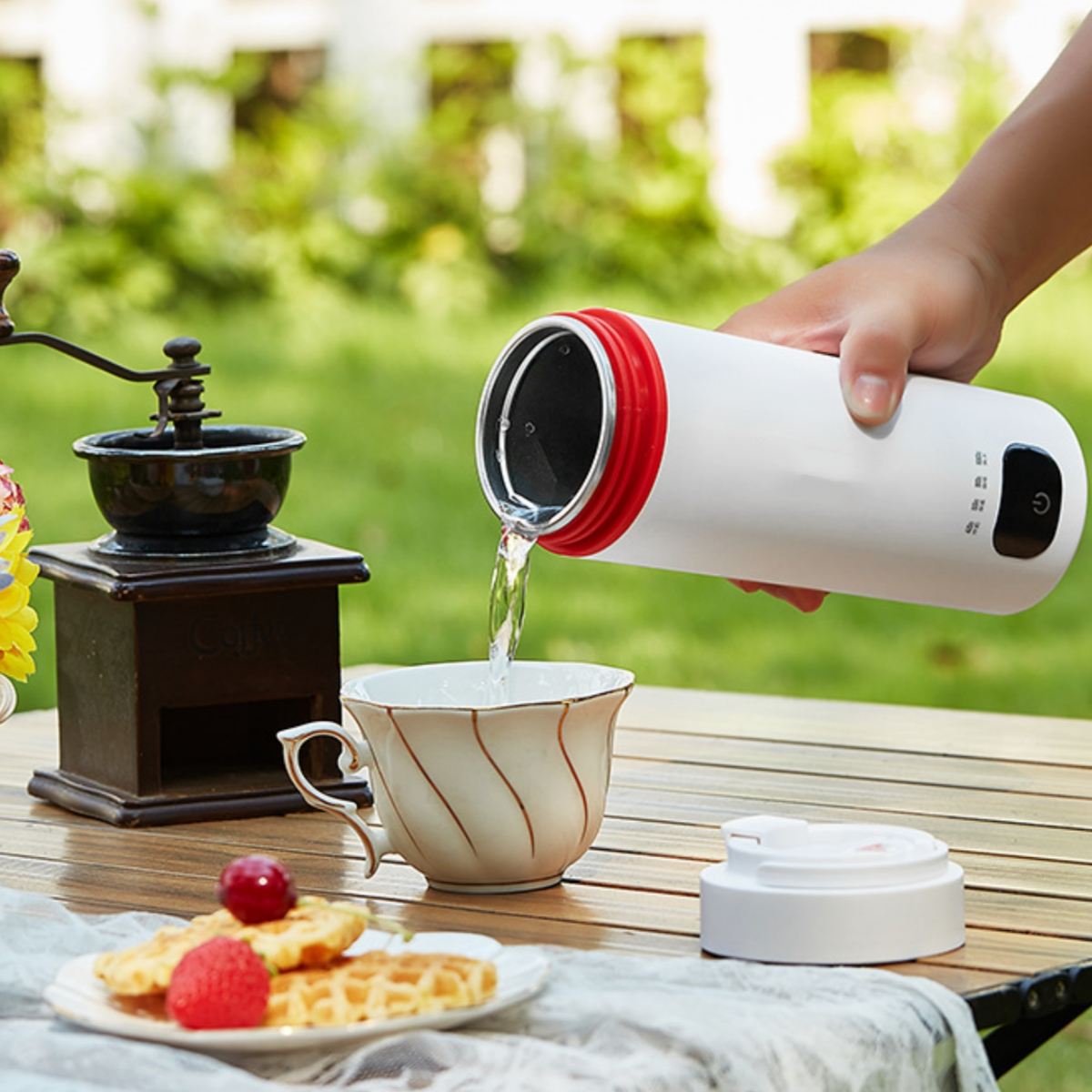 Eine Person gießt Wasser in eine Teetasse, mit Essen auf dem Tisch.