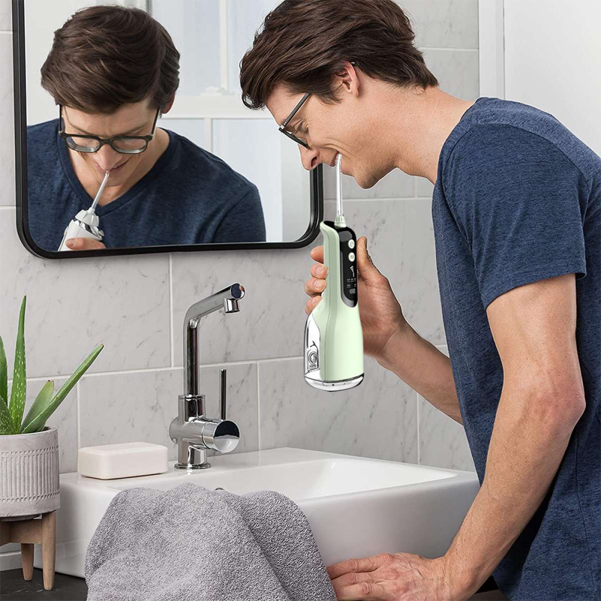 Mann benutzt einen grün-weißen Munddusche im Badezimmer. Spiegelbild sichtbar.