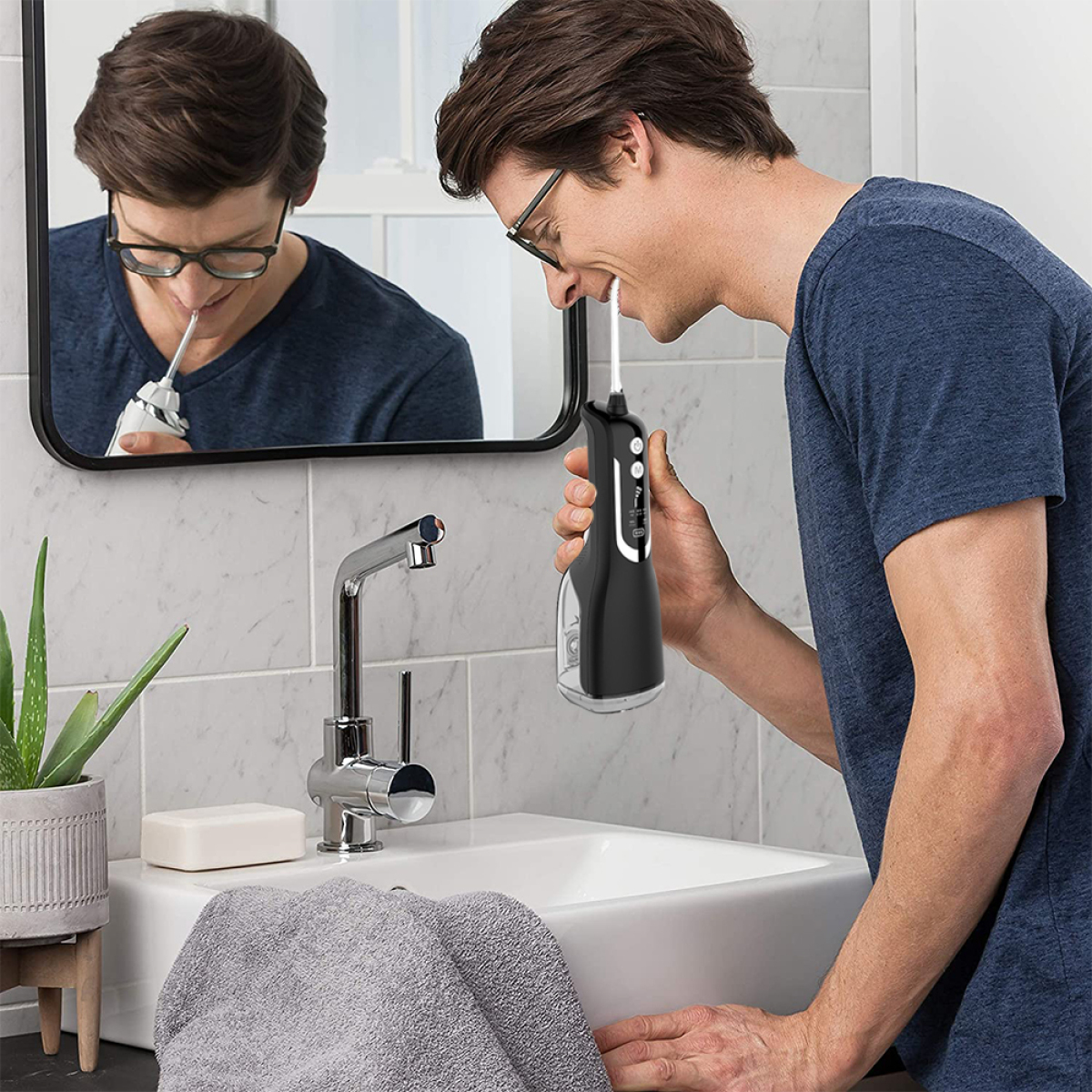 Mann benutzt im Badezimmer einen schwarzen Wasser-Flosser, im Spiegel über einem weißen Waschbecken.