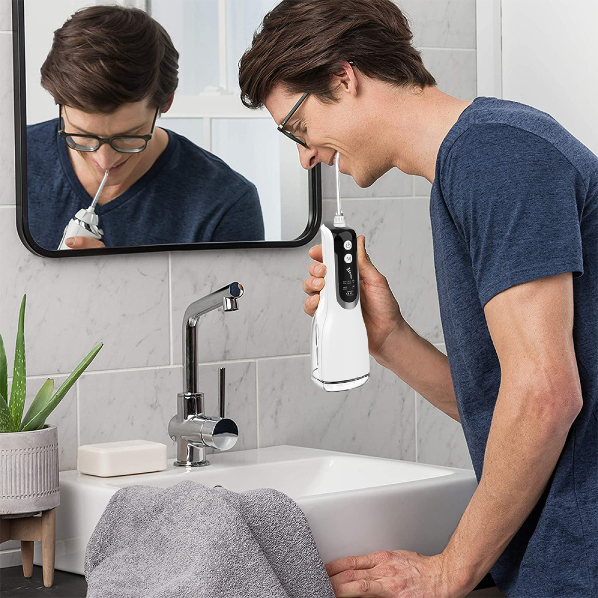 Mann benutzt einen Munddusche im Badezimmer. Spiegel und Waschbecken sind sichtbar.