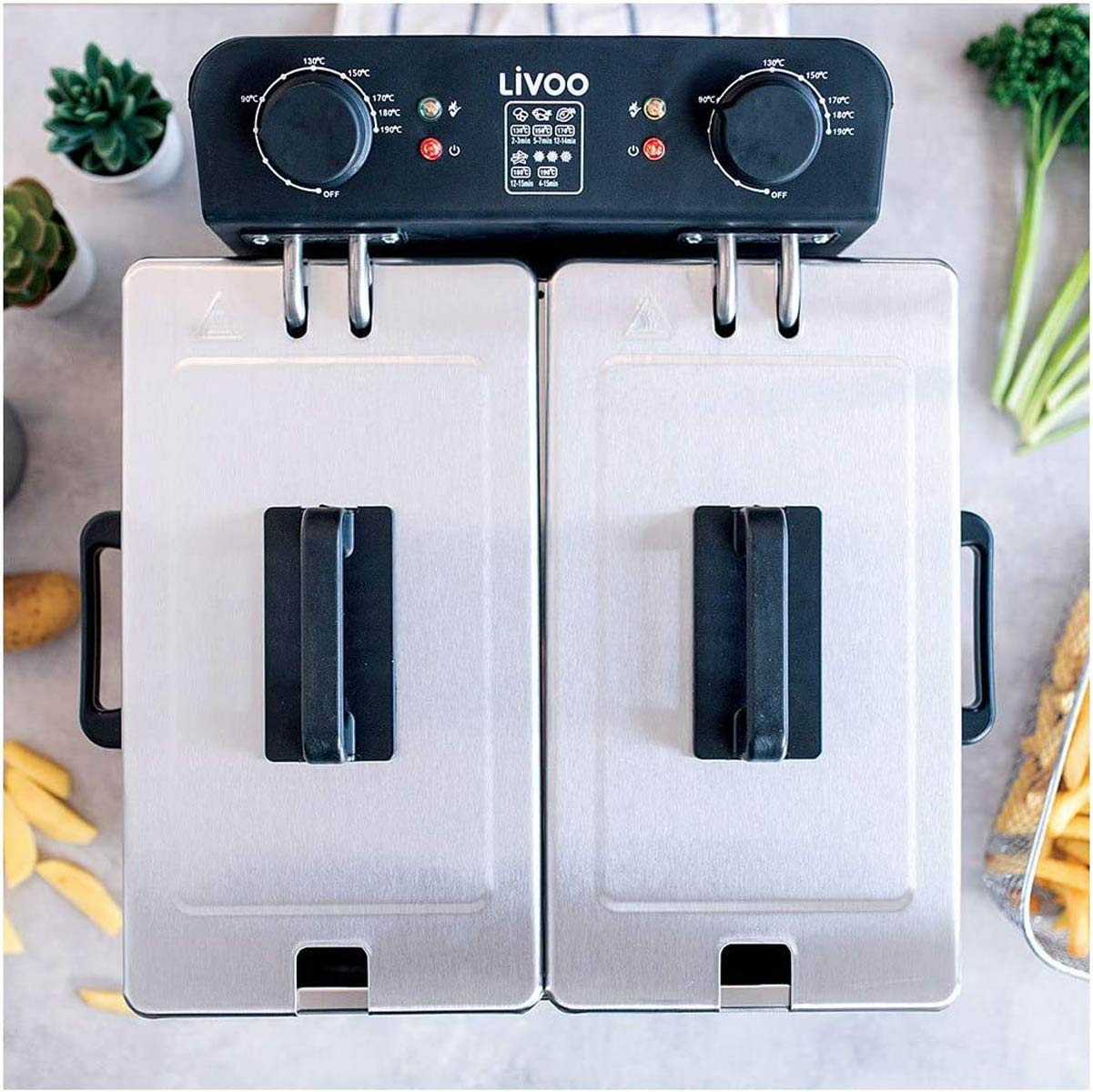 Widok z góry na podwójną frytkownicę z zamkniętymi pokrywami, otoczoną białą powierzchnią i frytkami.