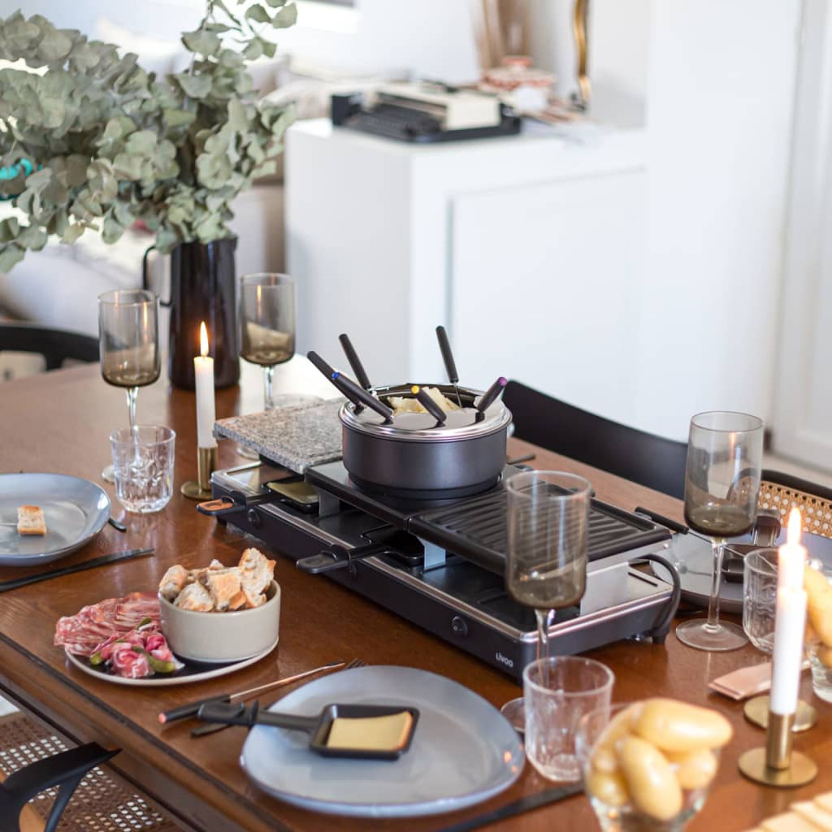 Un tavolo da pranzo apparecchiato per la fonduta. Include una pentola per fonduta, piatti, bicchieri, candele, pane e carne.