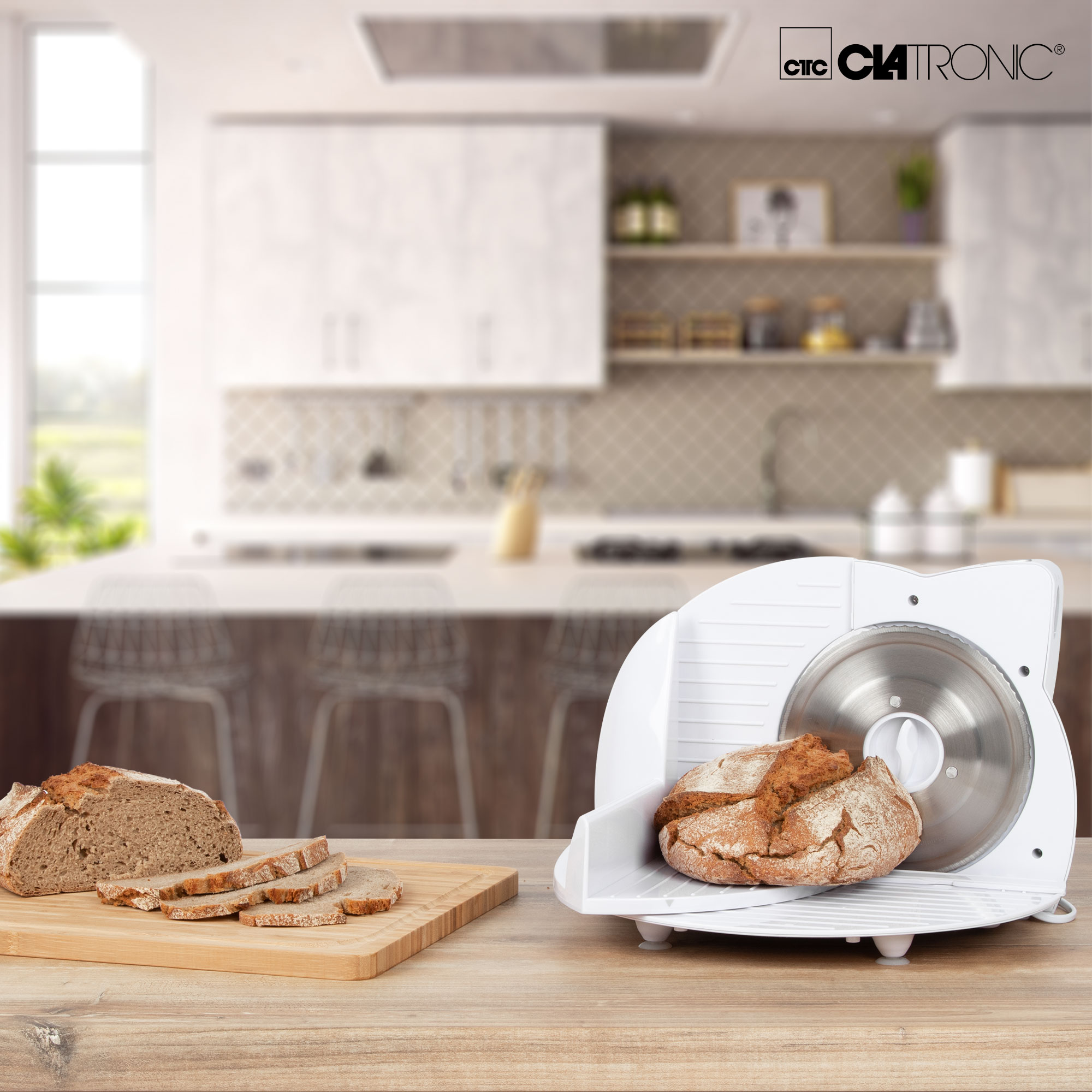 Biała krajalnica do chleba z chlebem na drewnianym stole, kuchnia w tle.