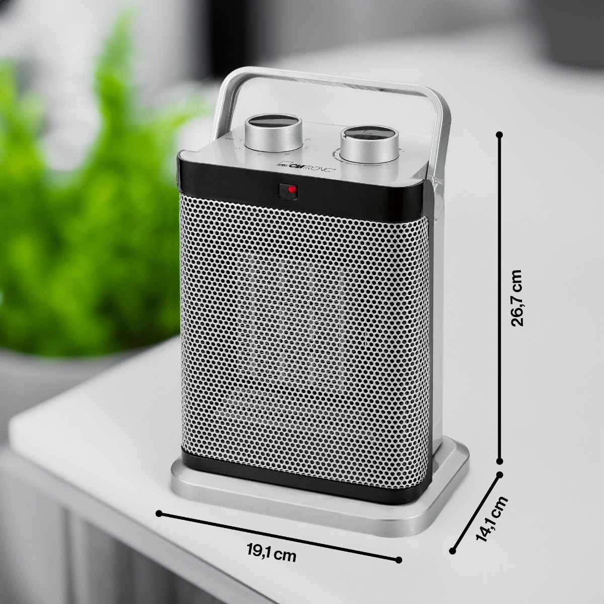 Srebrno-czarny grzejnik z wymiarami na białym stole obok rośliny.