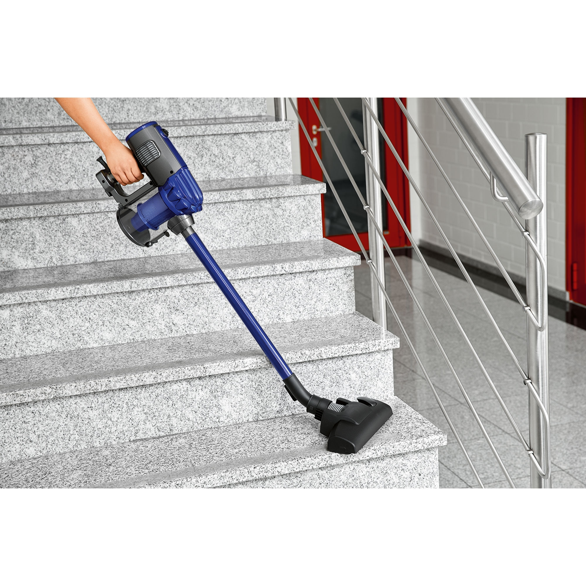 Osoba odkurzająca schody niebiesko-czarnym odkurzaczem.