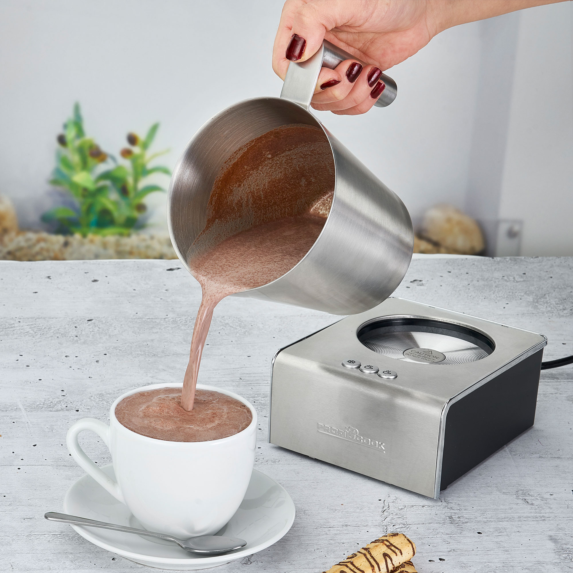 Osoba nalewa czekoladę z metalowego dzbanka do filiżanki na spodku.