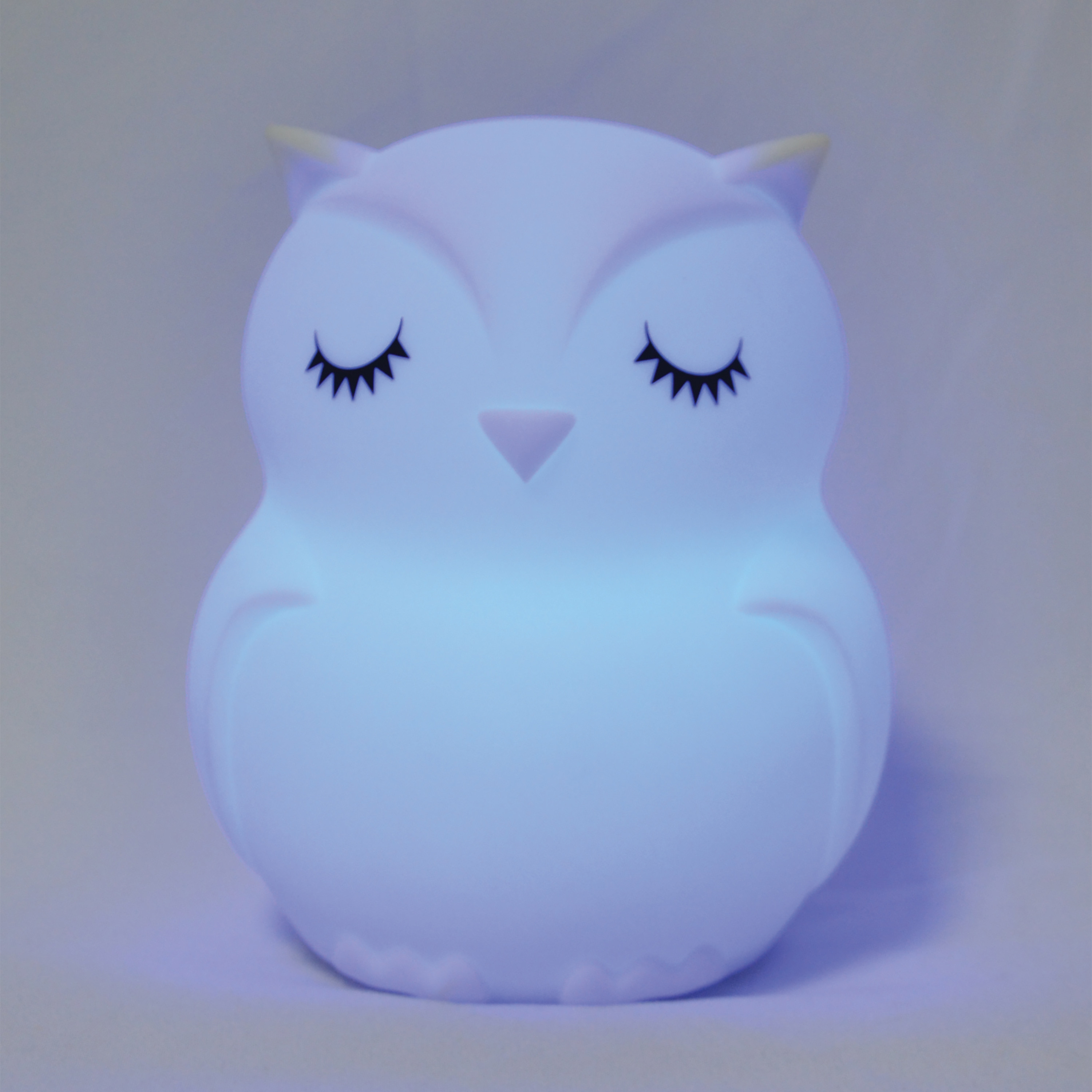 Luz nocturna con forma de búho, blanca con brillo azul, ojos cerrados, sobre fondo morado.