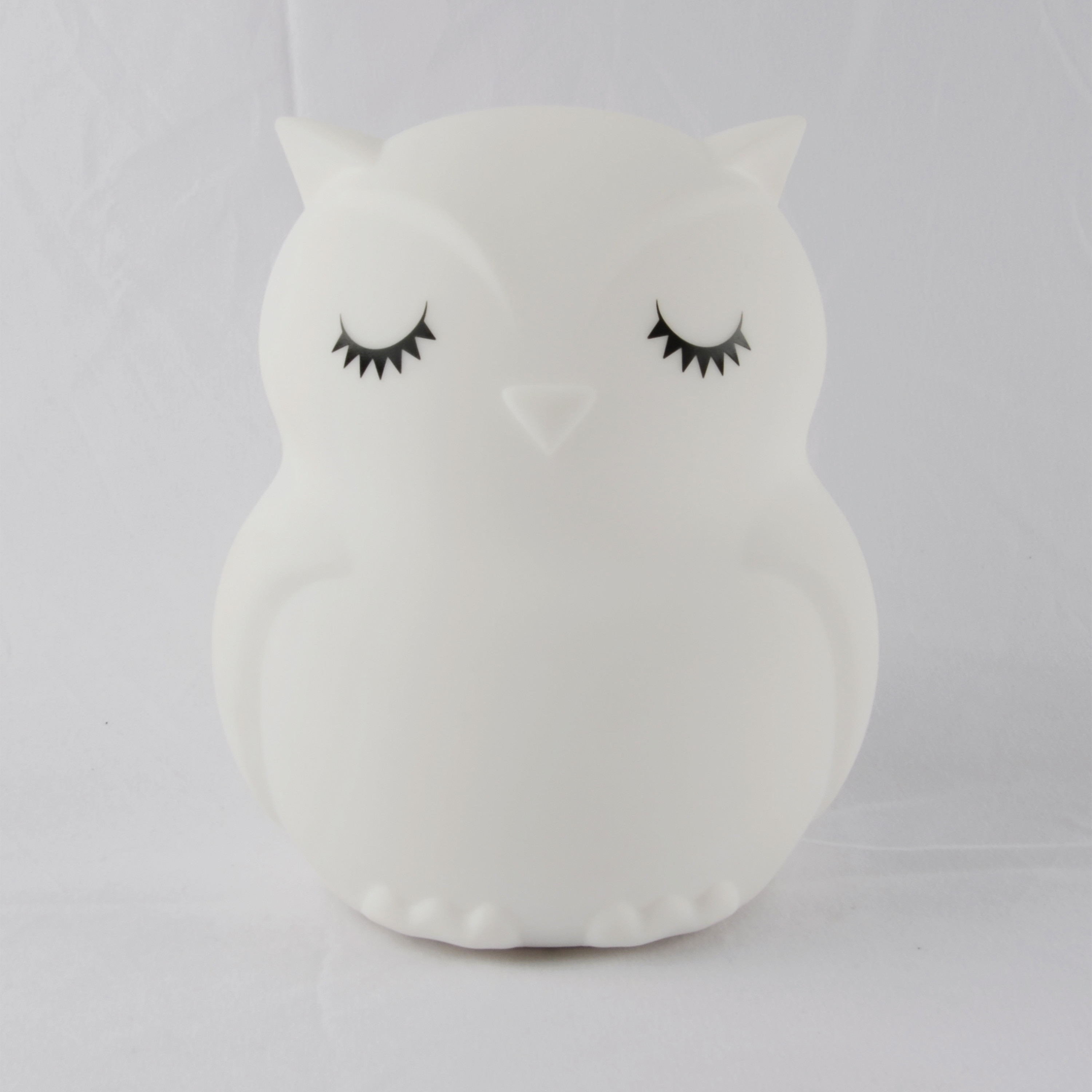 Luz de noche blanca con forma de búho y ojos cerrados. Fondo blanco.