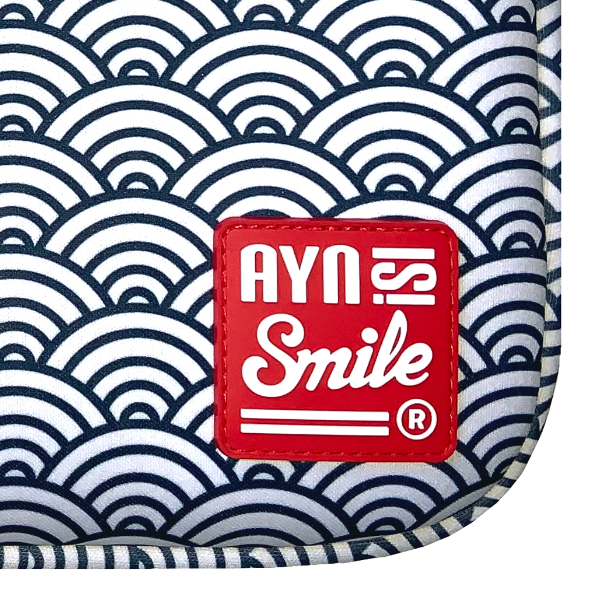 Un parche rojo con texto blanco 'AYNS Smile' sobre un fondo estampado blanco y azul marino.