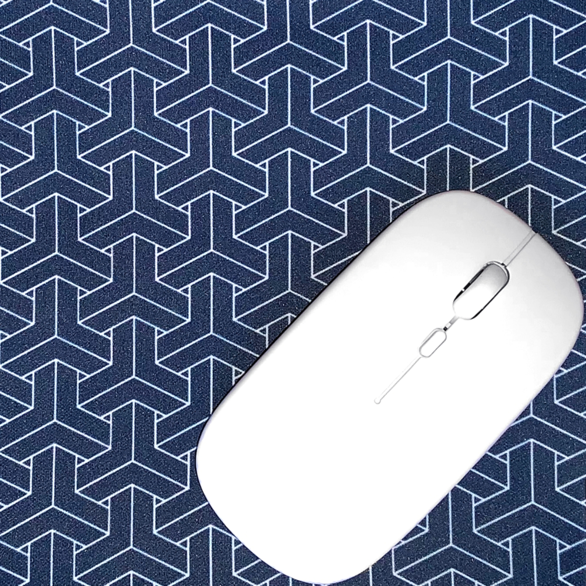Ratón inalámbrico blanco sobre alfombrilla con patrón geométrico azul. El ratón tiene rueda.