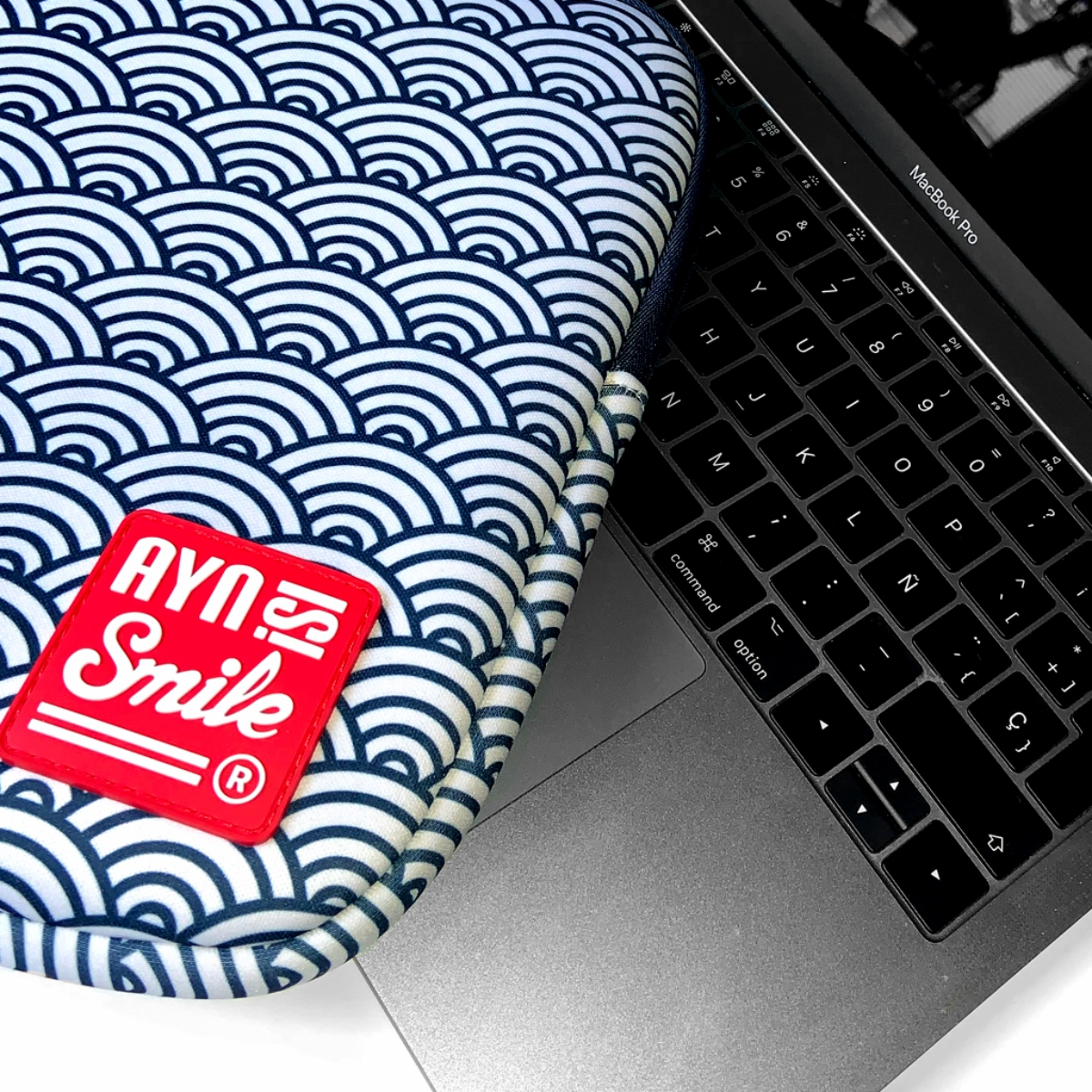 Un portátil con una funda estampada y un parche rojo que dice 'Ayn Smile'.