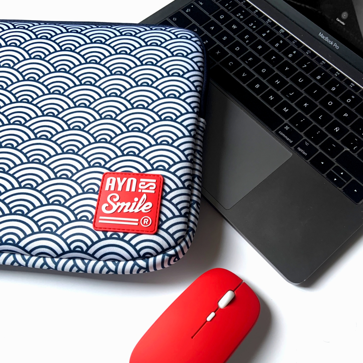 Laptop, funda y ratón rojo. La funda tiene un patrón de olas azules y blancas. El ratón es rojo.