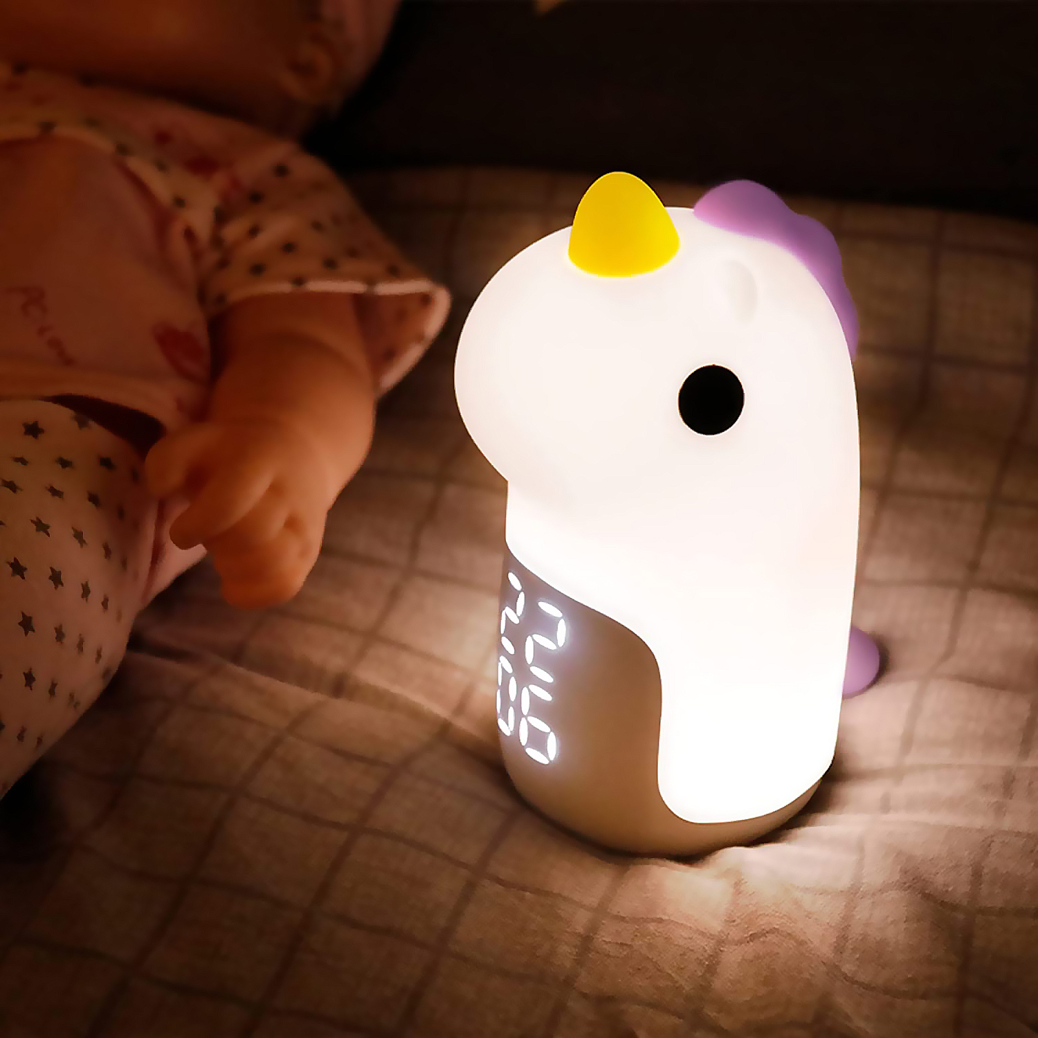 Una luz de noche de unicornio blanco brillante con una pantalla de reloj digital. El fondo es una cama.