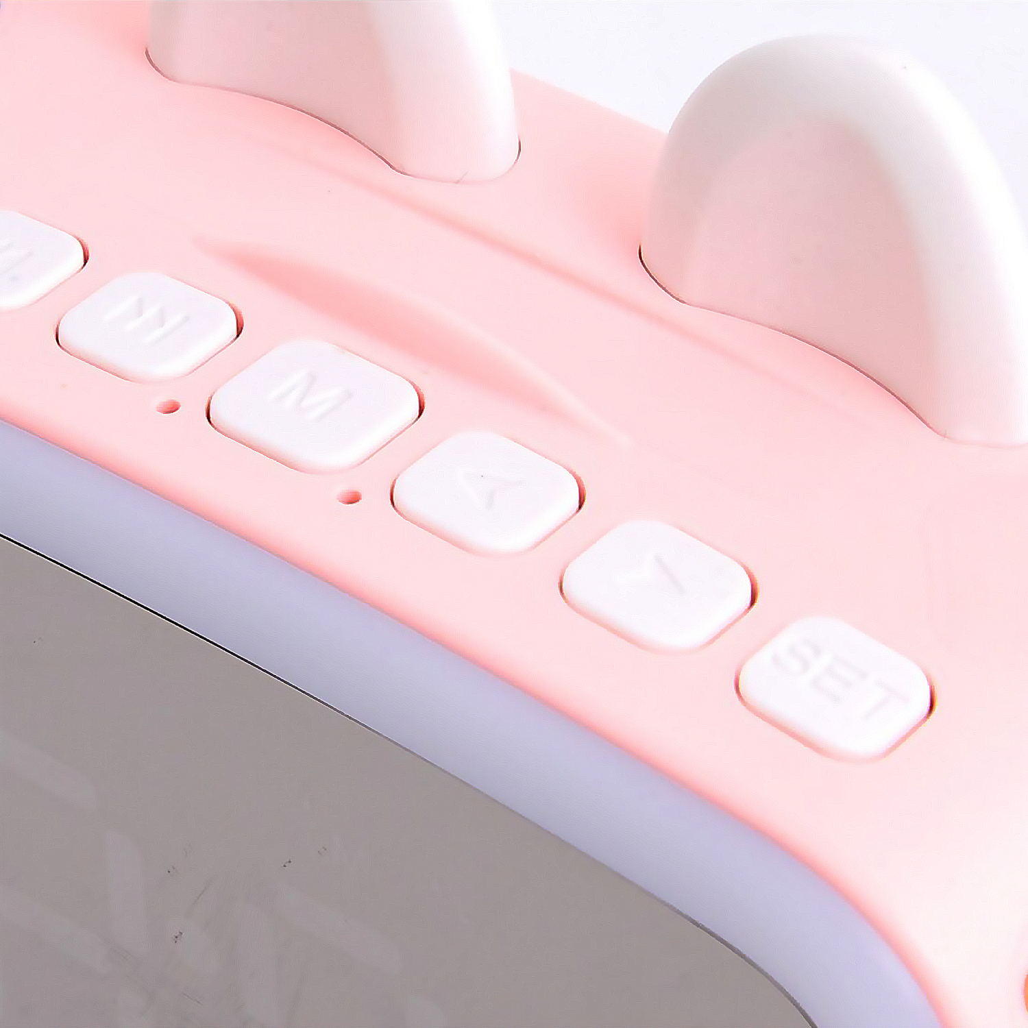 Primer plano de un despertador rosa con botones blancos. Los botones dicen M, flecha y set.