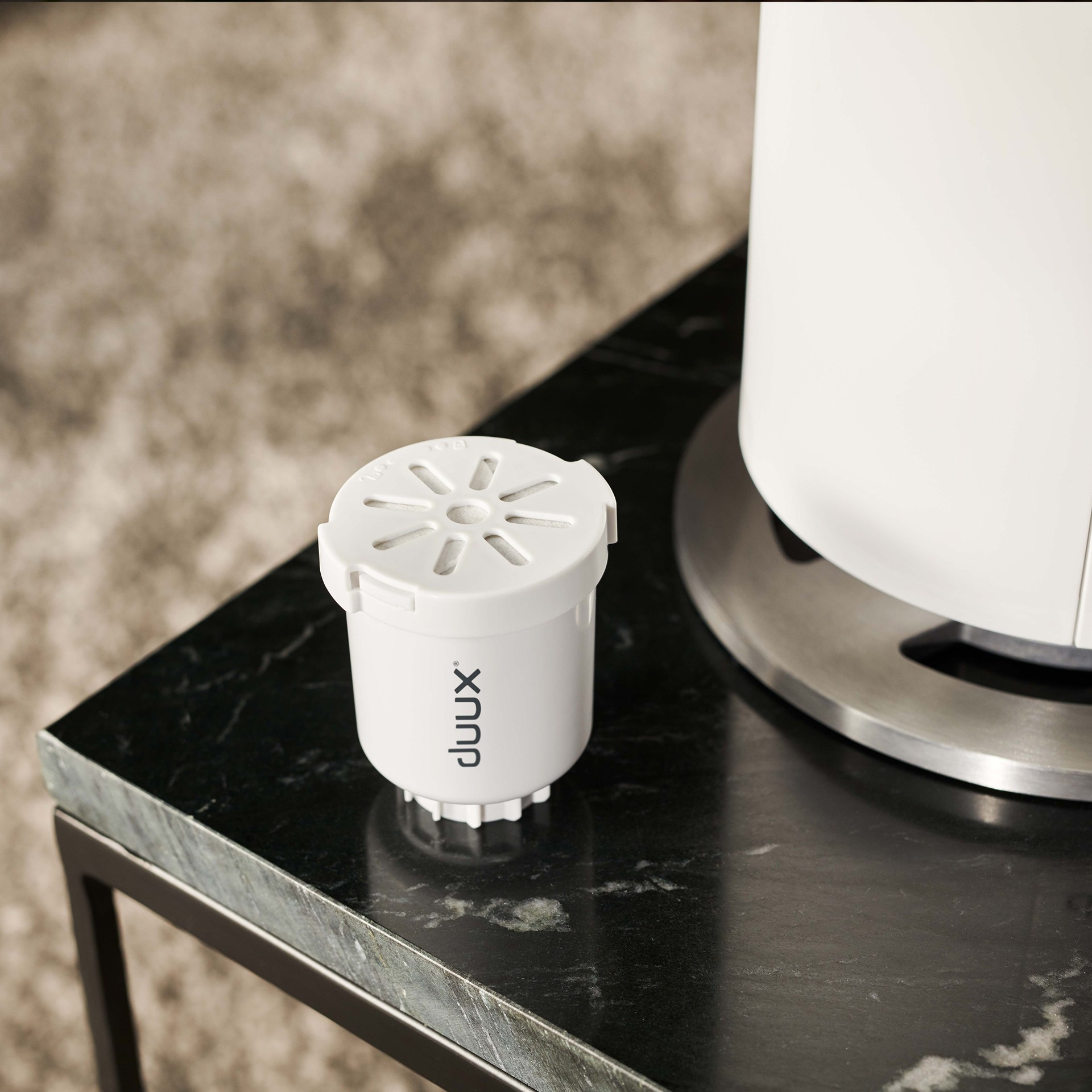 Biały filtr oczyszczacza powietrza na ciemnej marmurowej powierzchni z białą podstawą.