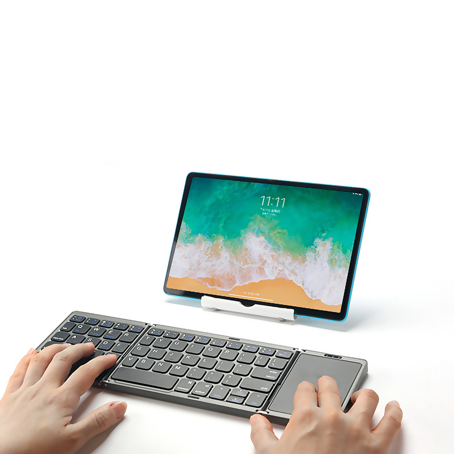 Tableta en soporte, teclado y manos de una persona escribiendo en el teclado.