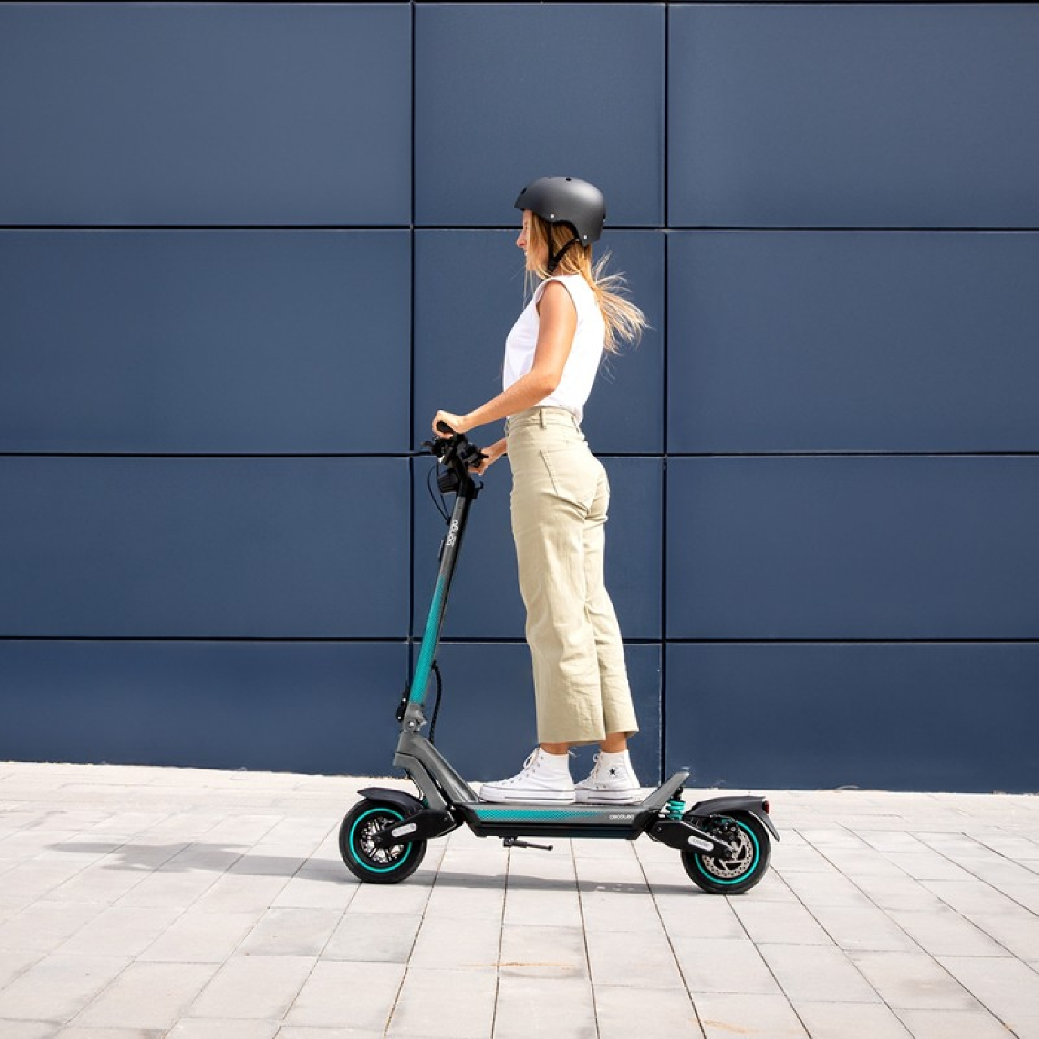 Mujer en un scooter, usando casco, frente a una pared azul.