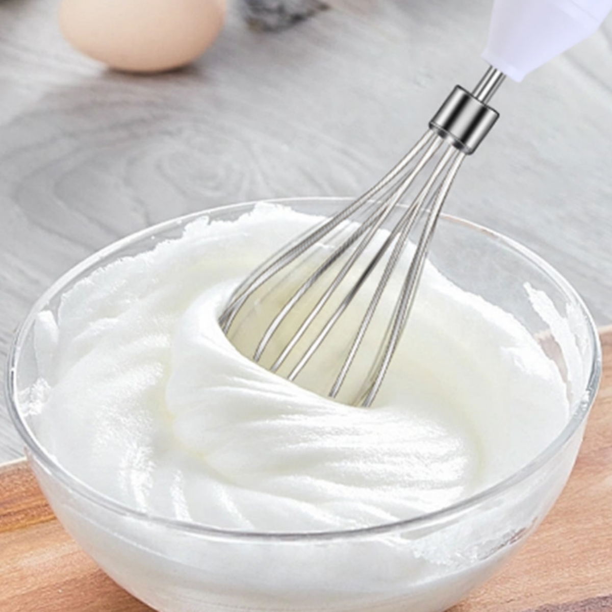 Ein Handmixer schlägt Sahne in einer Glasschüssel auf einer Holzoberfläche.