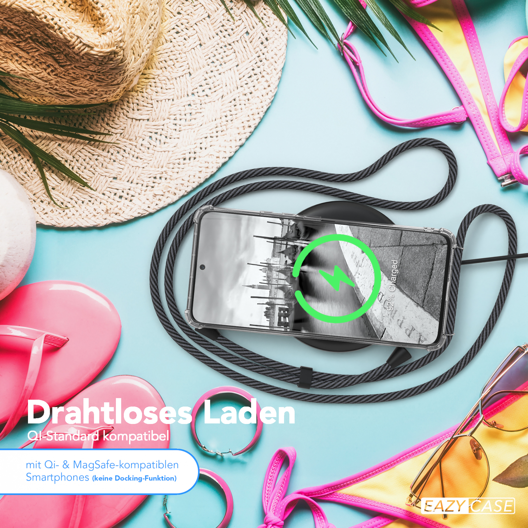 Telefon auf Ladegerät, umgeben von Accessoires, Strohhut und Sonnenbrille.