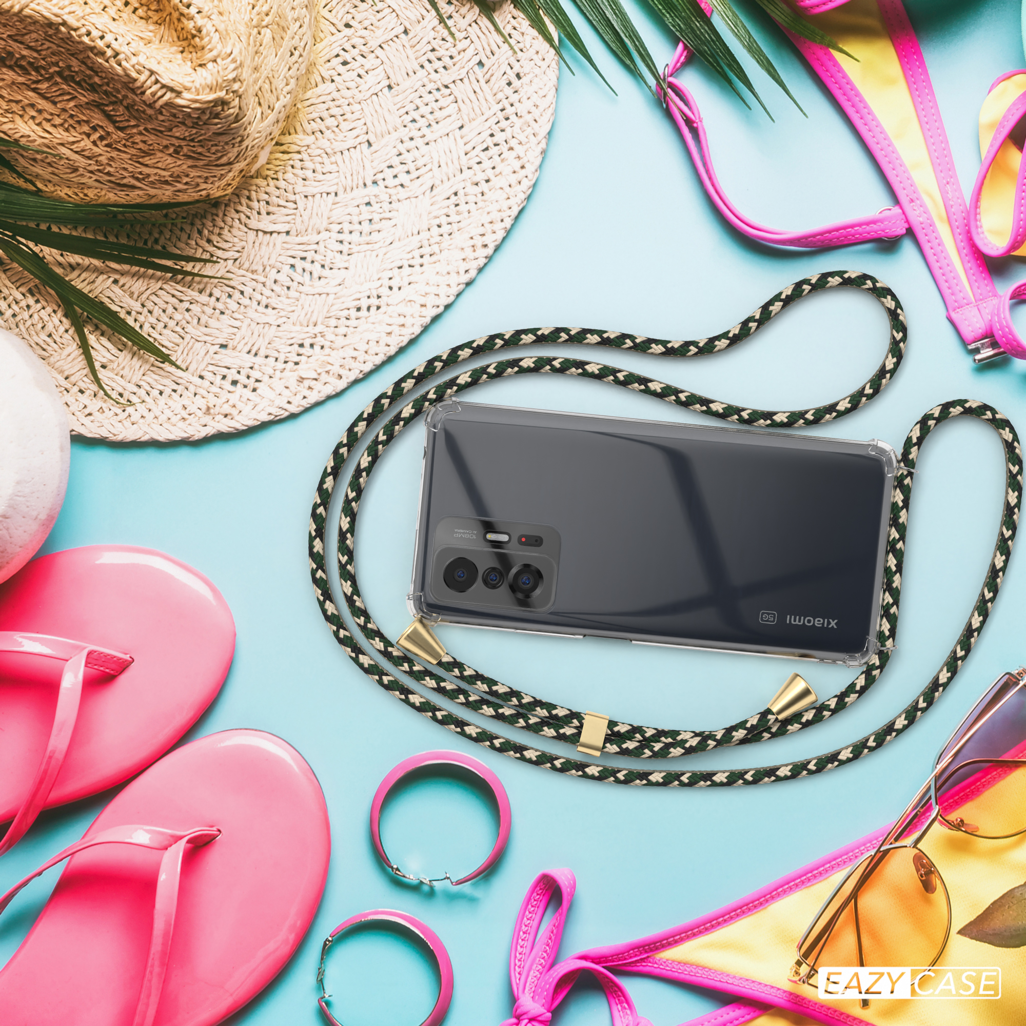 Telefon mit klarer Hülle und grünem, schwarzem und goldenem Lanyard auf blauem Hintergrund. Strandartikel sind herum.