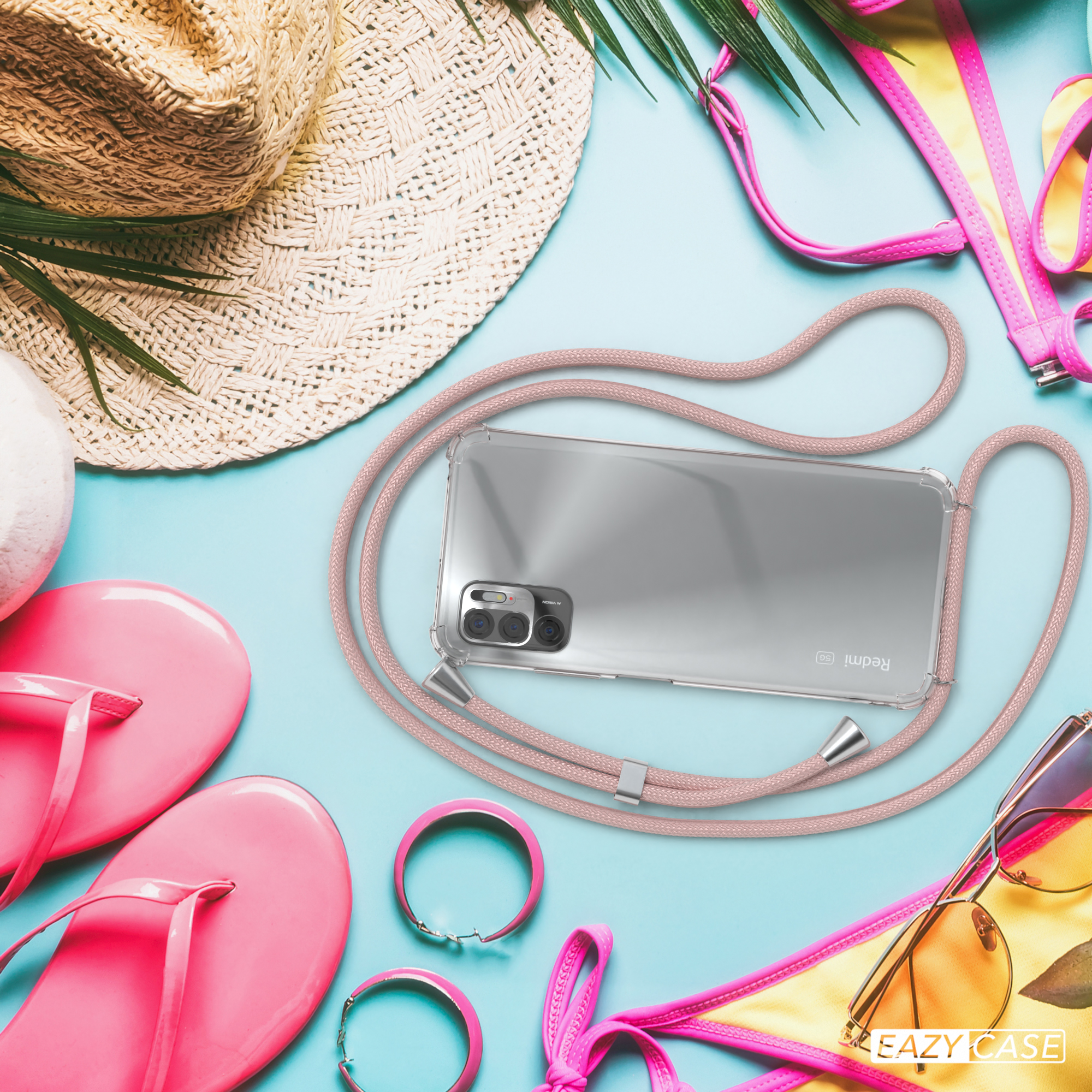Telefon mit Hülle und Gurt am Strand mit Accessoires wie Sandalen und einem Hut.