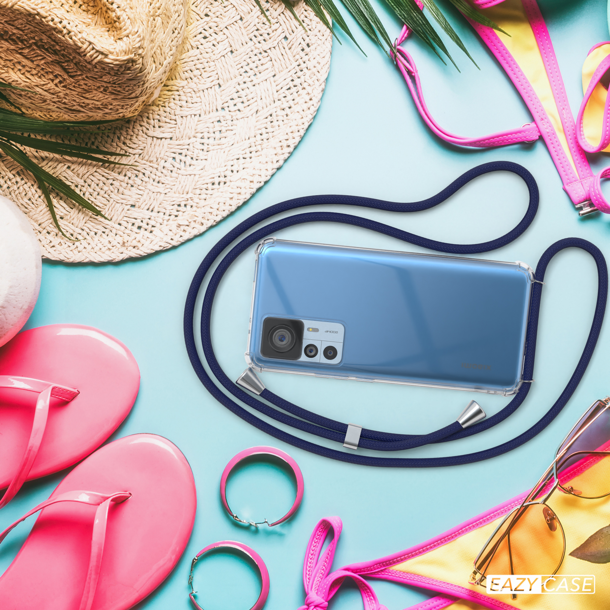 Ein Telefon in einer Hülle mit einem Band liegt auf einer blauen Oberfläche, mit Sommeraccessoires.