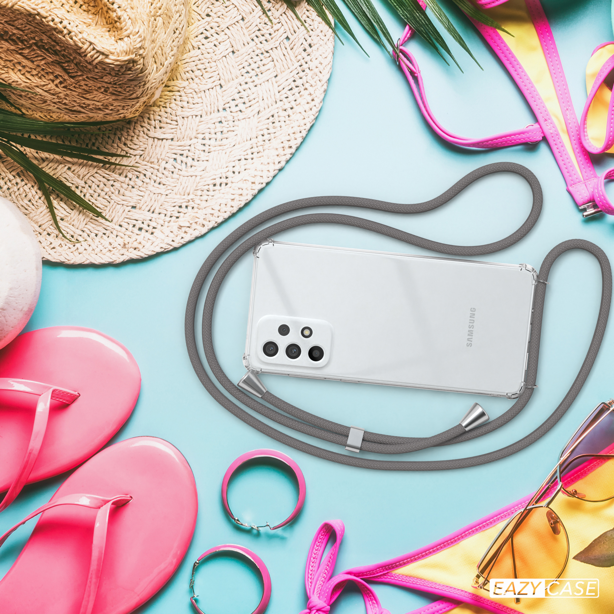 Telefon in Hülle mit grauem Lanyard, umgeben von Strandutensilien: Flip-Flops, Sonnenbrille, Strohhut auf blauem Hintergrund.