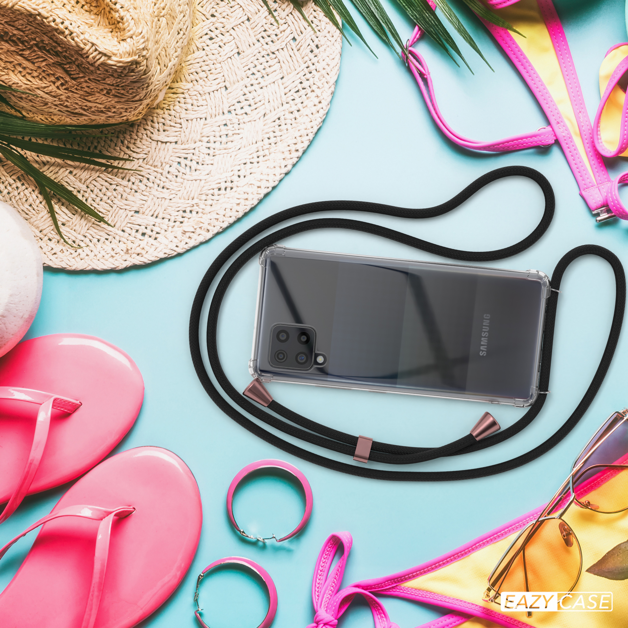 Telefon in einer transparenten Hülle mit schwarzem Riemen und rosa Akzenten, liegt auf einem Strandhintergrund.