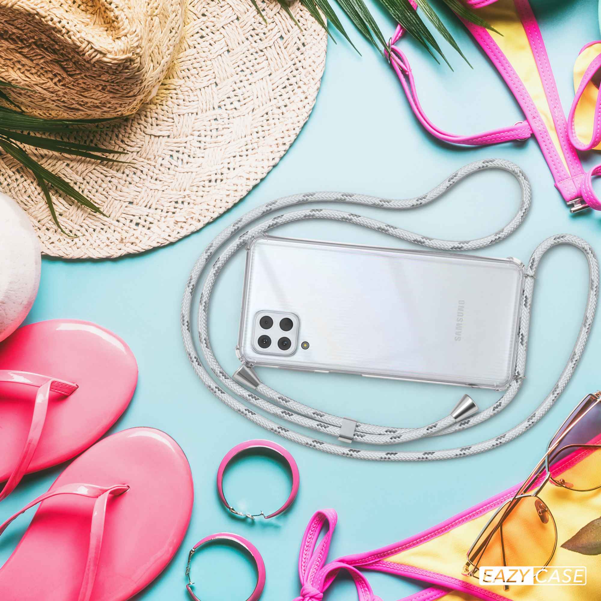 Telefon mit Hülle am Strand mit Accessoires wie Hut, Sonnenbrille und rosa Gegenständen.