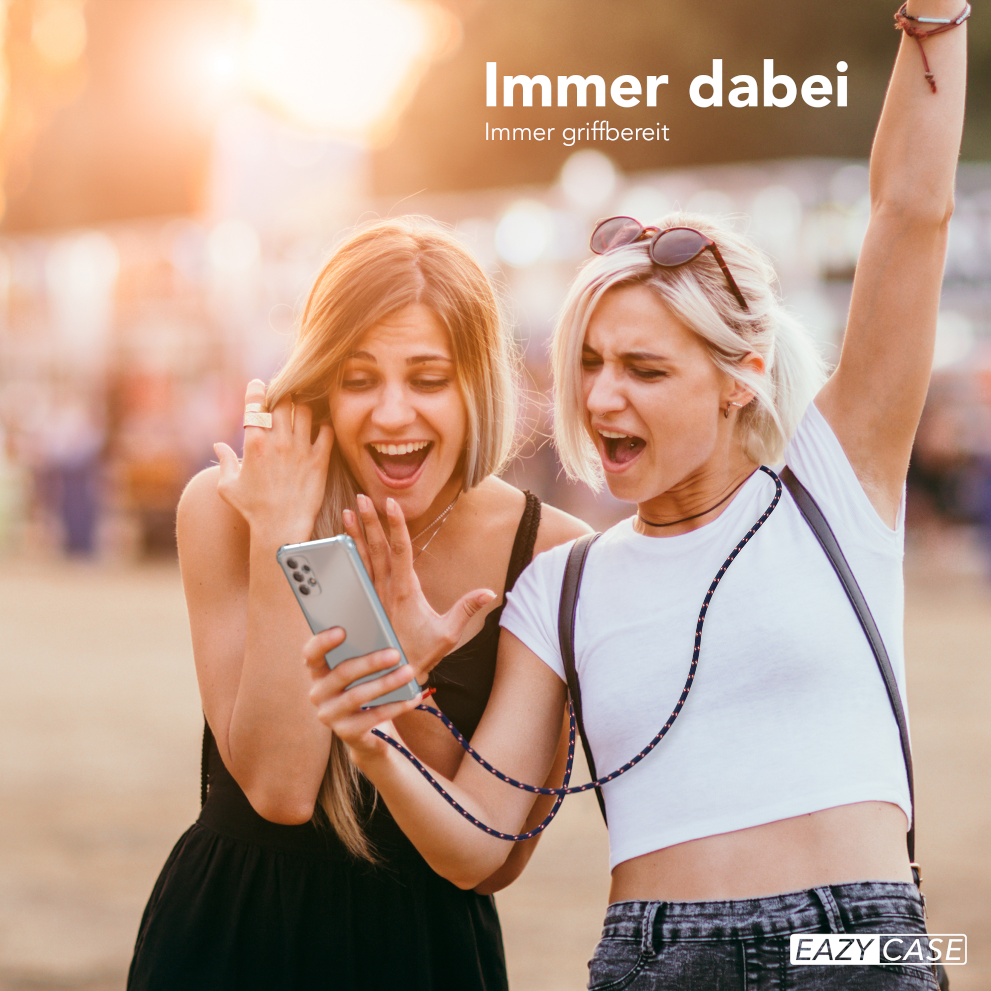 Zwei aufgeregte Frauen schauen auf ein Telefon mit Kordel. Sonnenuntergang im Hintergrund. Text: Immer dabei.